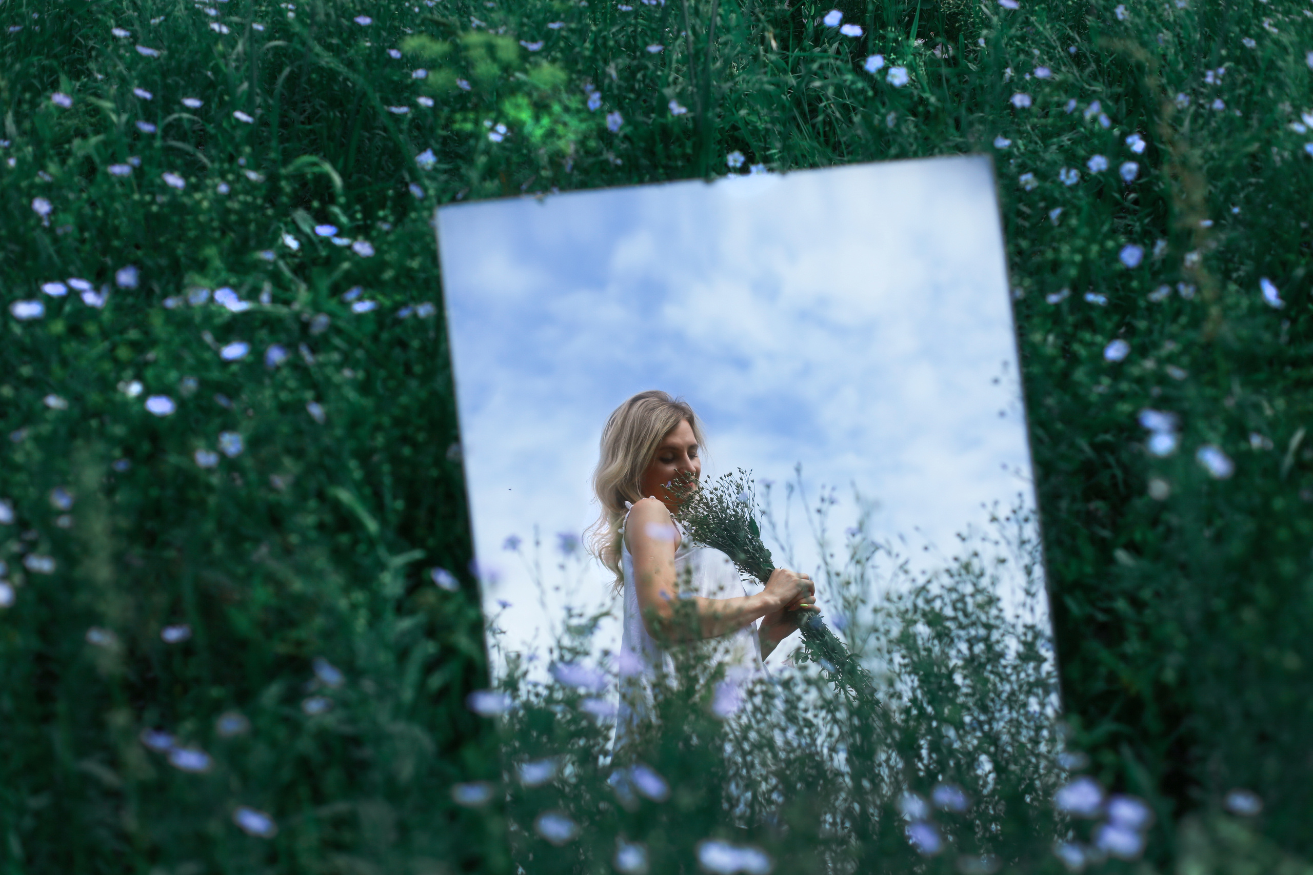 Отражение в зеркале девушки с букетом цветов в руках.