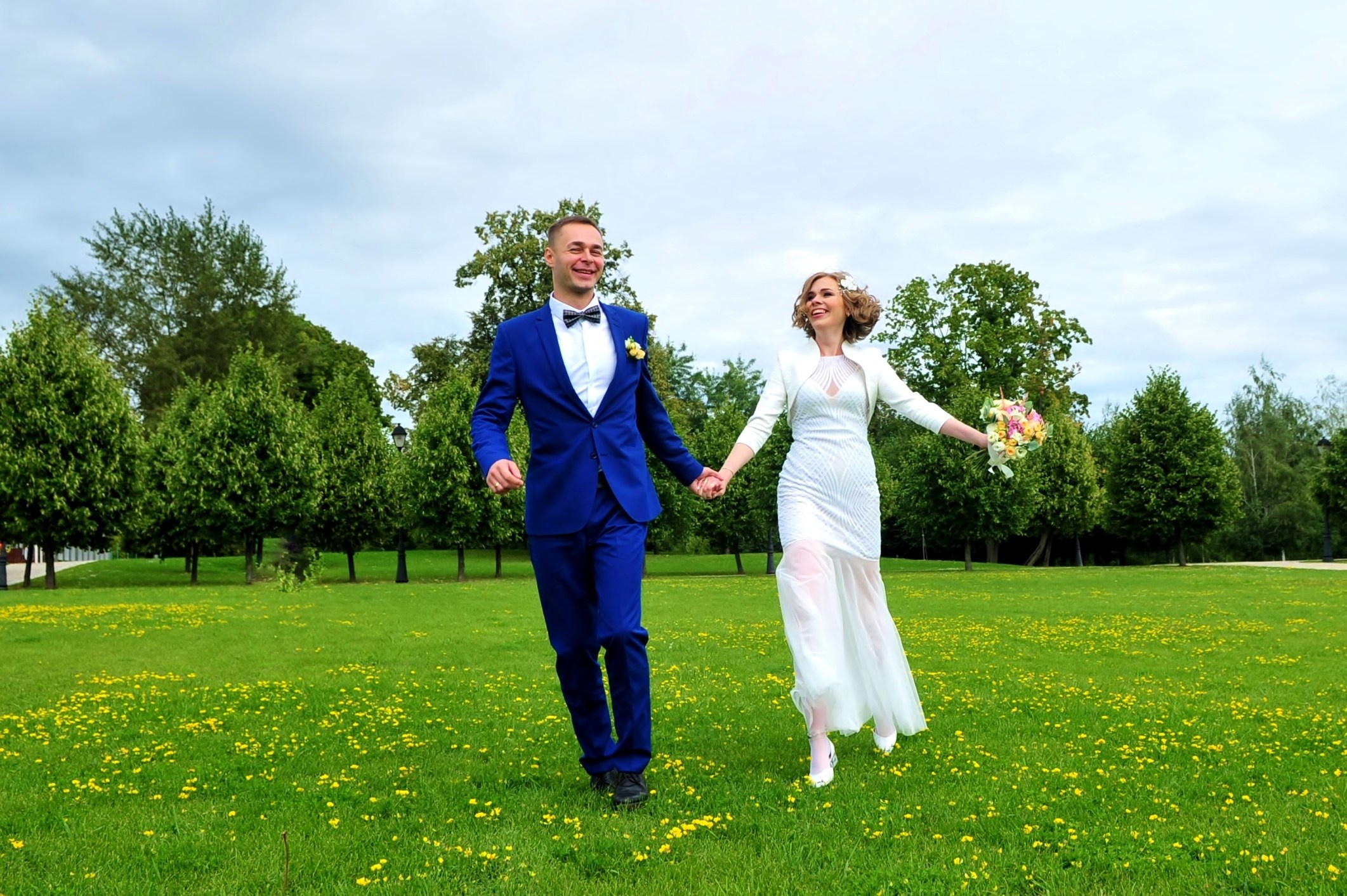 Свадьба в Царицыно хмурым прохладным летним днём, жених с невестой бегут по зеленой траве в парке