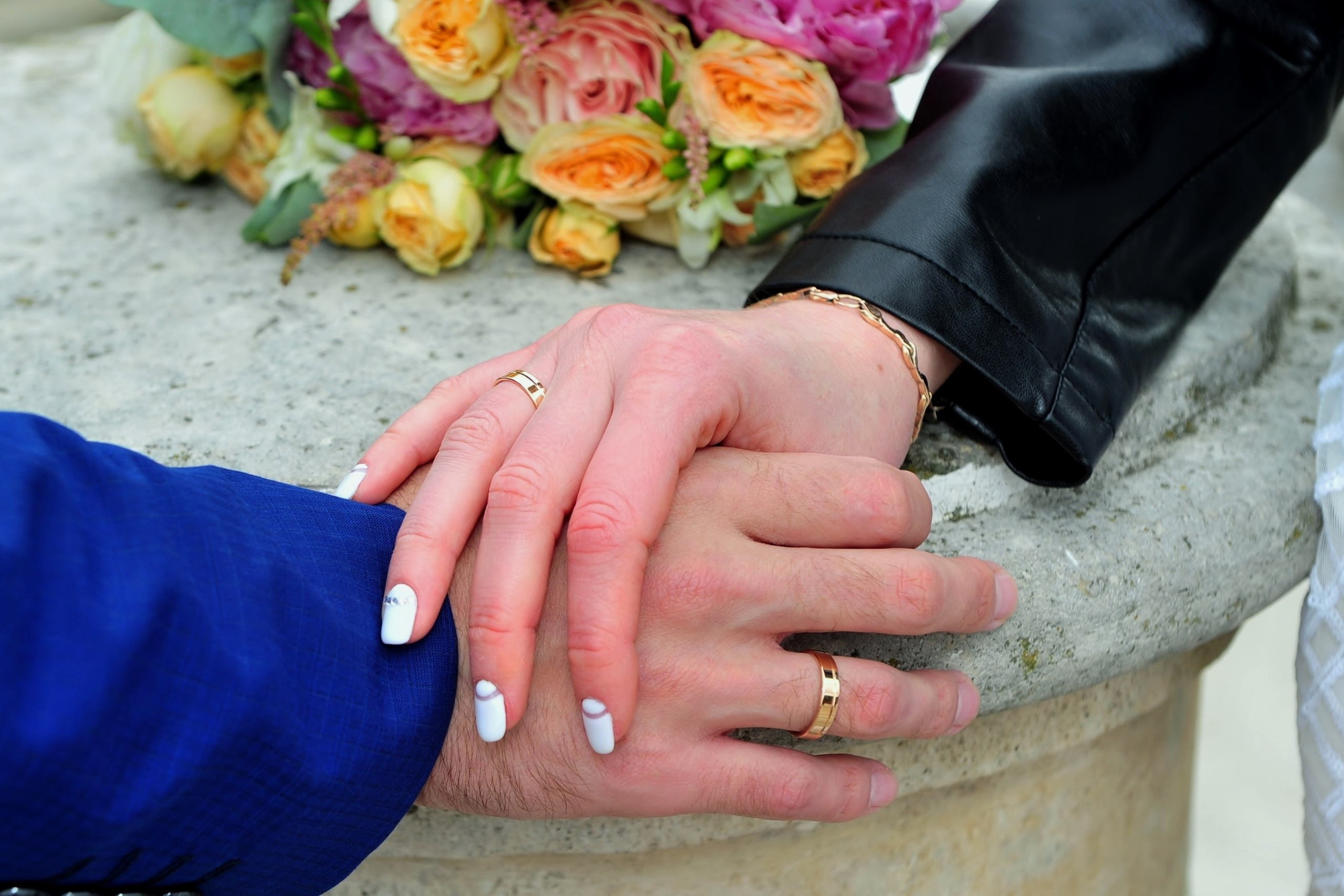 Свадьба в Царицыно хмурым прохладным летним днём, руки новобрачных лежат на белом камне моста, позади рук лежит букет невесты