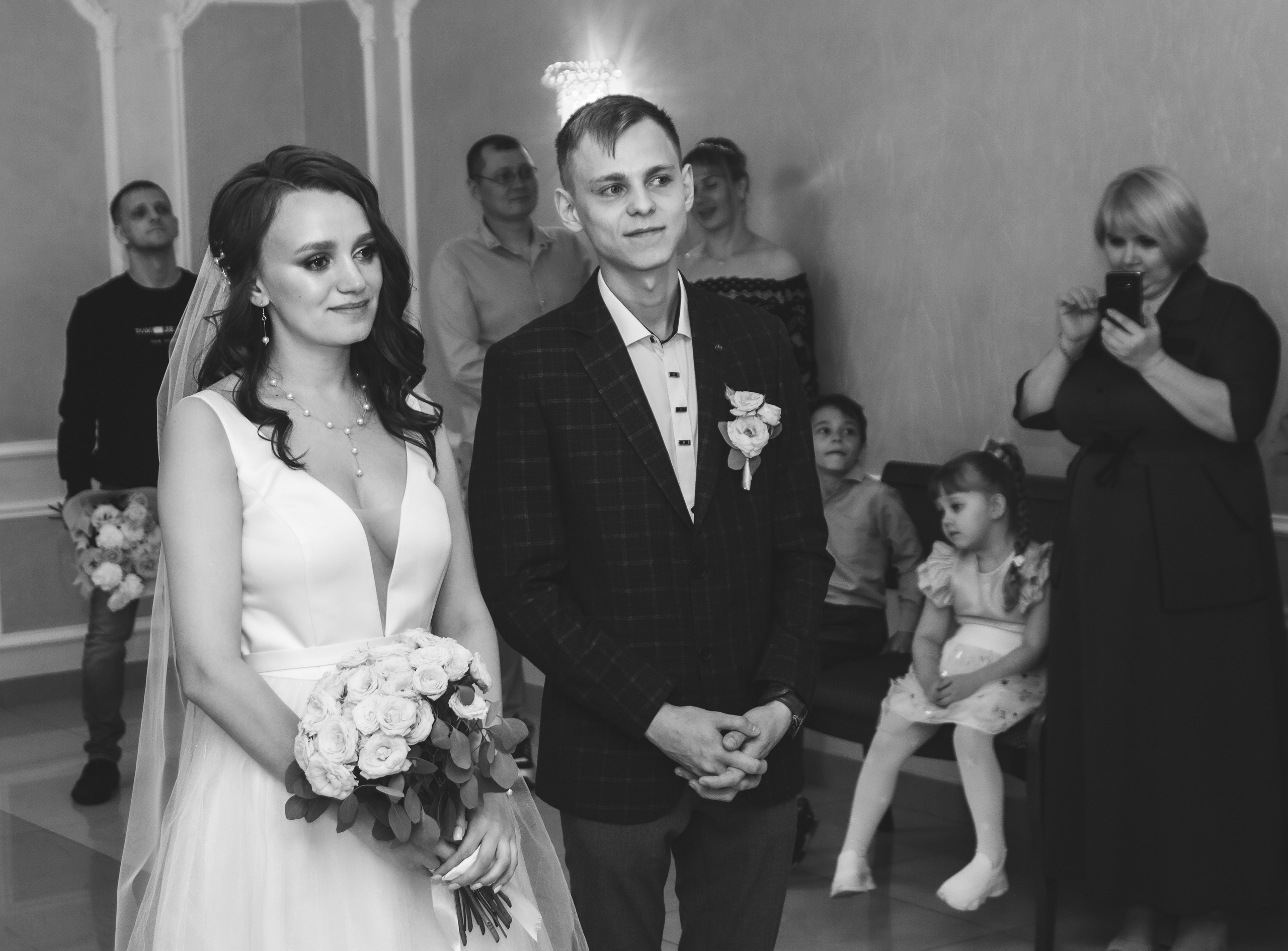 Чёрно-белое фото — жених и невеста стоят в торжественном зале, рядом гости.