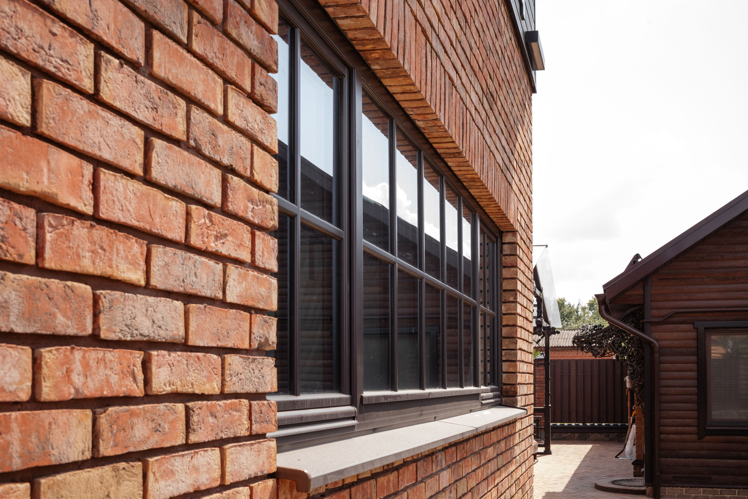 Фасад гаража с панорамными окнами и деревянной облицовкой. Стиль Лофт подчеркивает индустриальную эстетику и уют.