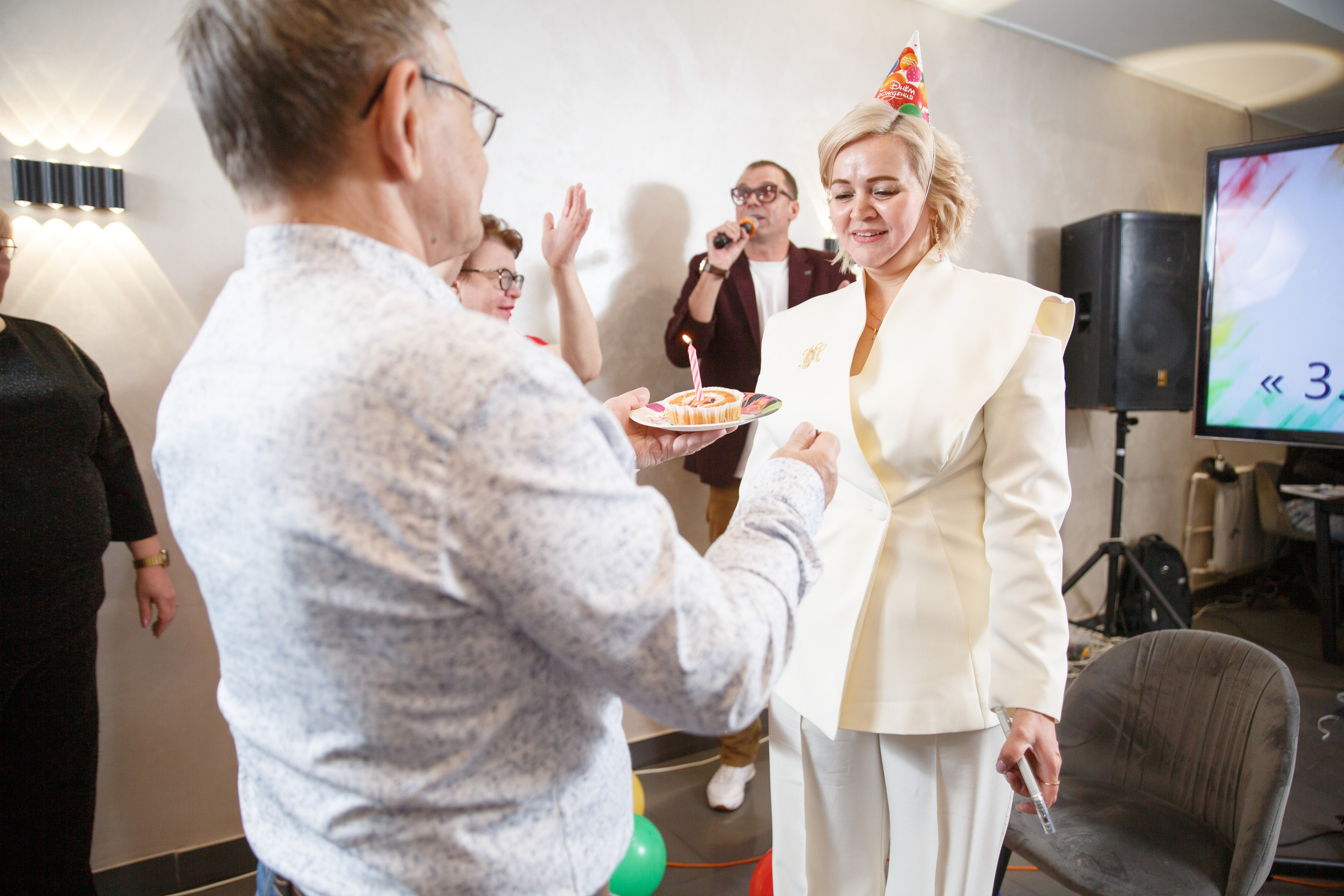 Мужчина поздравляет женщину в белом у праздничного стола.