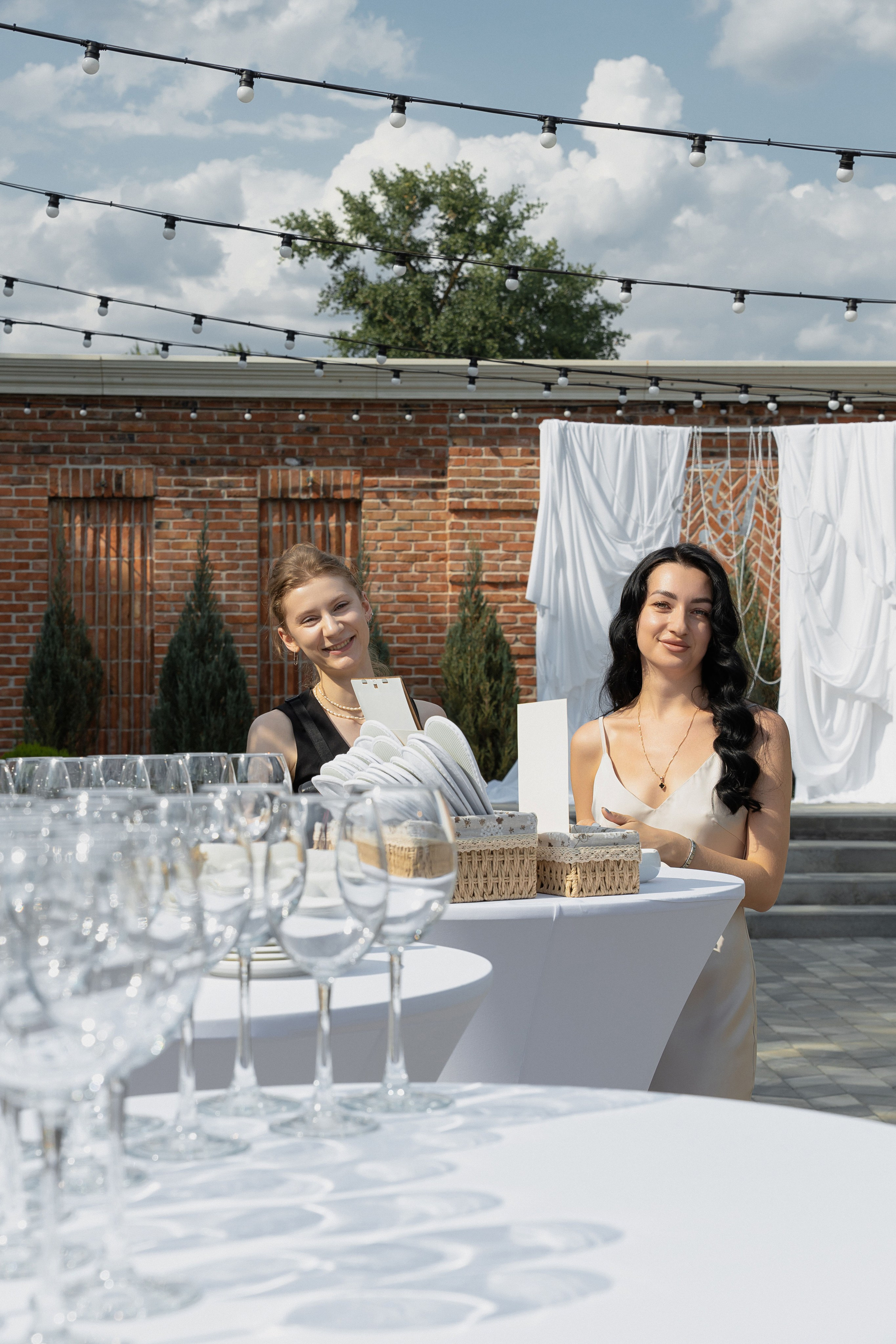 Гости на свадебной церемонии улыбаются у фуршетного стола с бокалами и тарелками на открытом воздухе