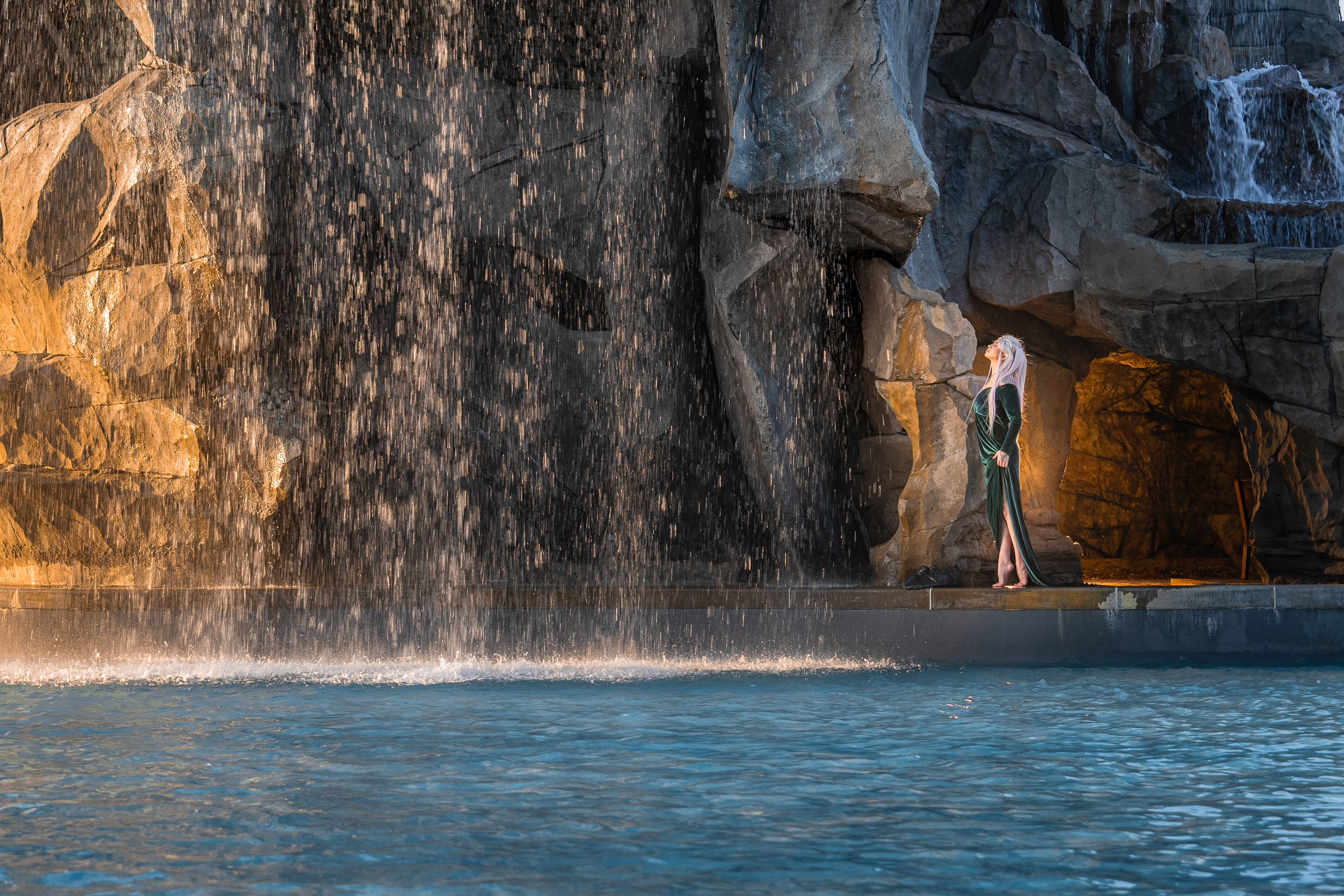 Женщина в белом купальнике под искусственным водопадом на территории замка Гарибальди, добавляющем динамику и волшебство в кадр.