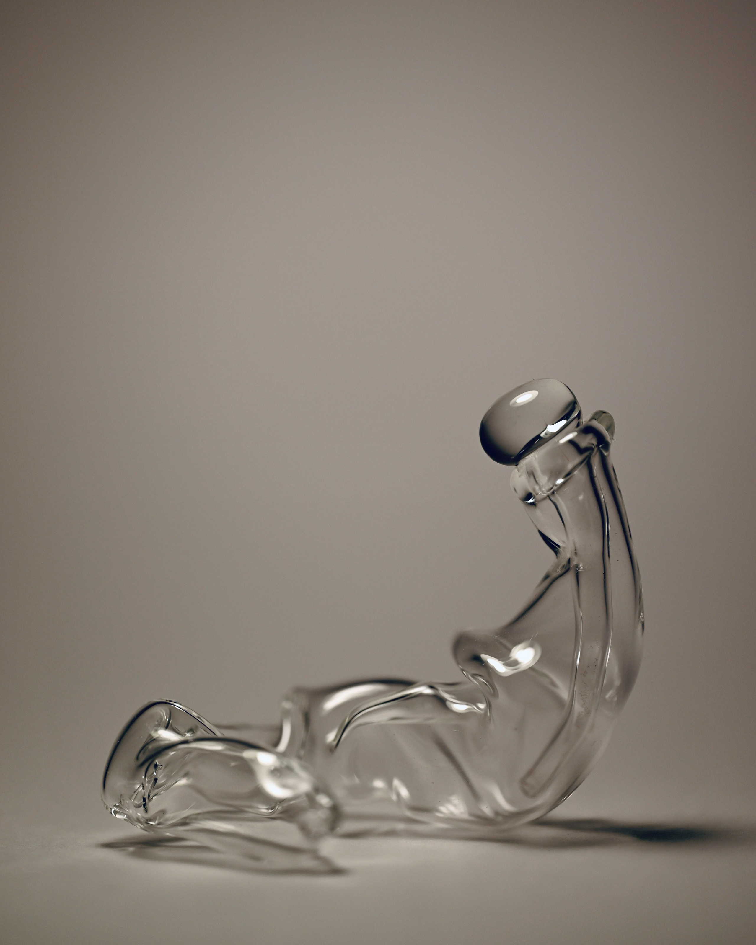 Флакон «Лень». Боросиликатное стекло. 2025 г.Флакон «Лень» - это форма, уставшая быть формой. Он отказался от усилия, позволил себе стекать, тянуться. Он не хочет быть «правильным» сосудом, не держит спину прямо и не стремится к симметрии. Он — как тело в утренней постели, как мысль, не вставшая с дивана. В «Лени» — смелость покоя. Она про внутреннее разрешение: быть неэффективным, быть собой.Стекло, податливое огню, здесь стало телом, выбравшим отдых вместо действия.