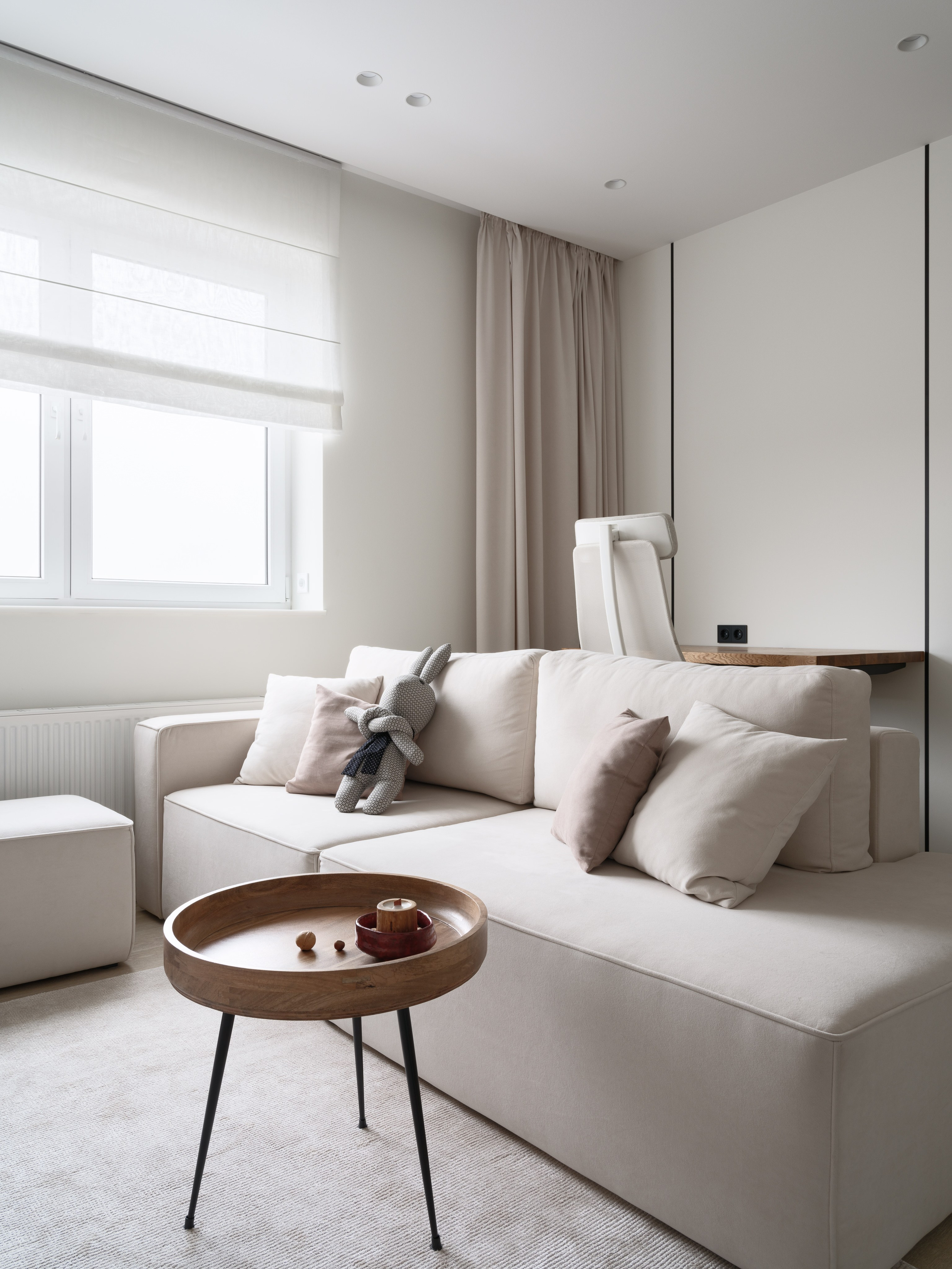 Современная гостиная в стиле минимализм: бежевый диван с подушками, римская штора, деревянный кофейный столик и уютный декор. Дизайн Евгении Княжевой и Владлены Приваловой, фото Сергея Денисенко