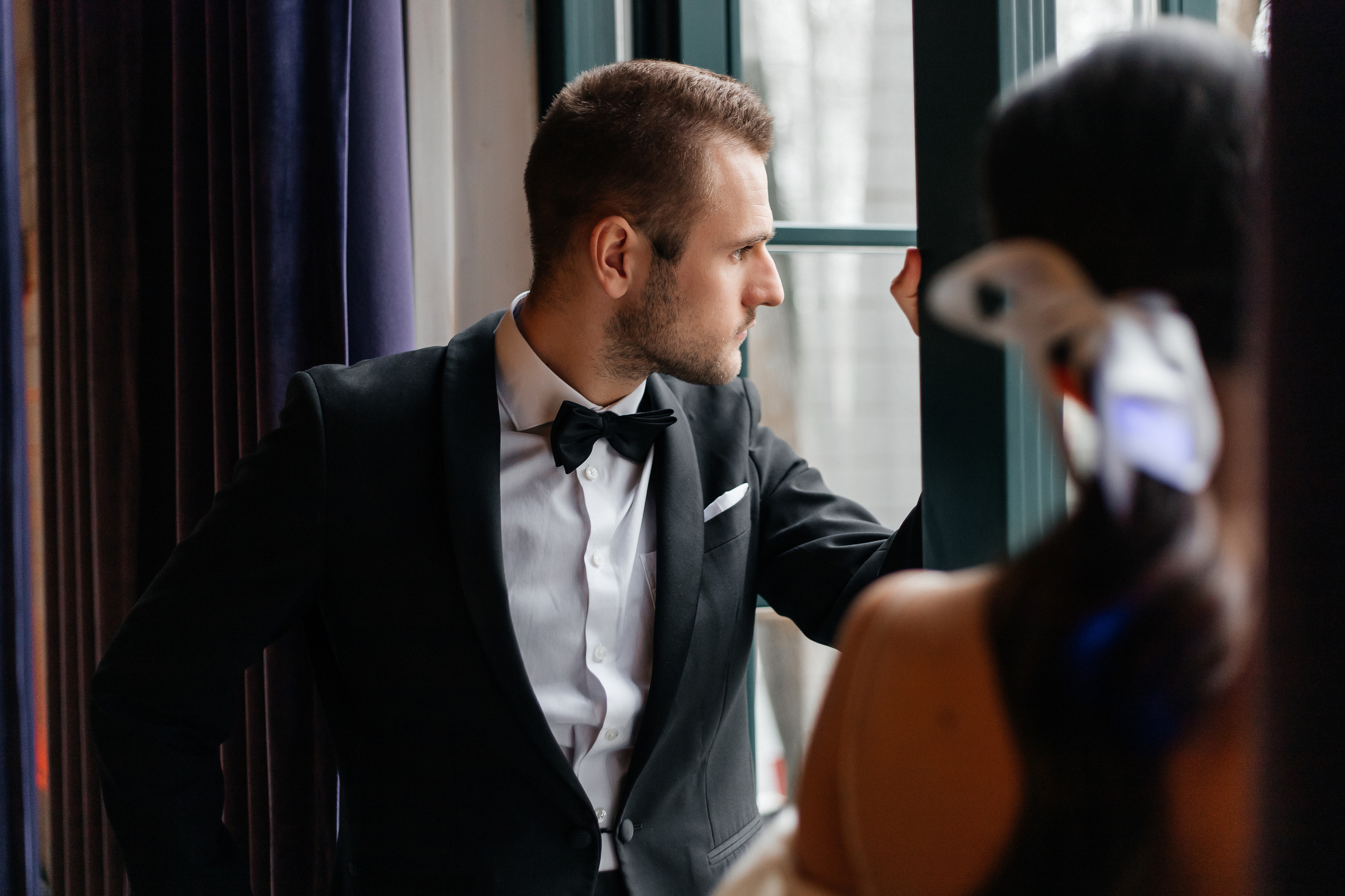 Жених в черном костюме смотрит  в окно