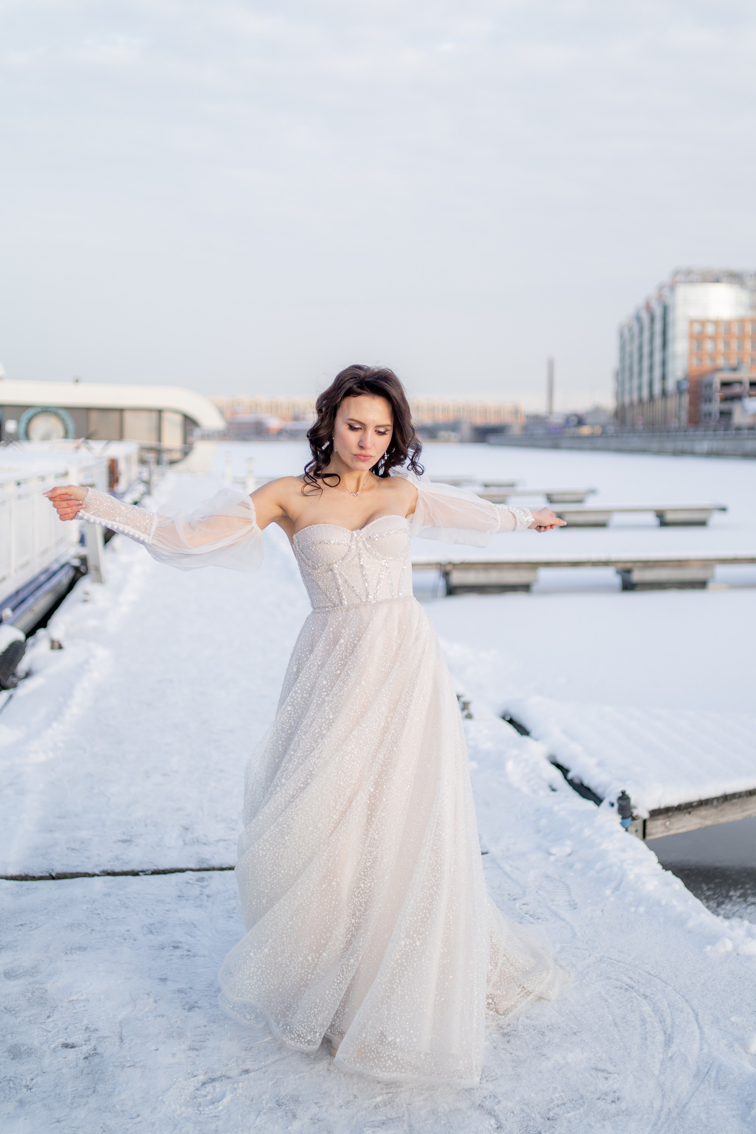 Невеста в свадебном платье танцует на снегу в яхт клубе на закате зимой