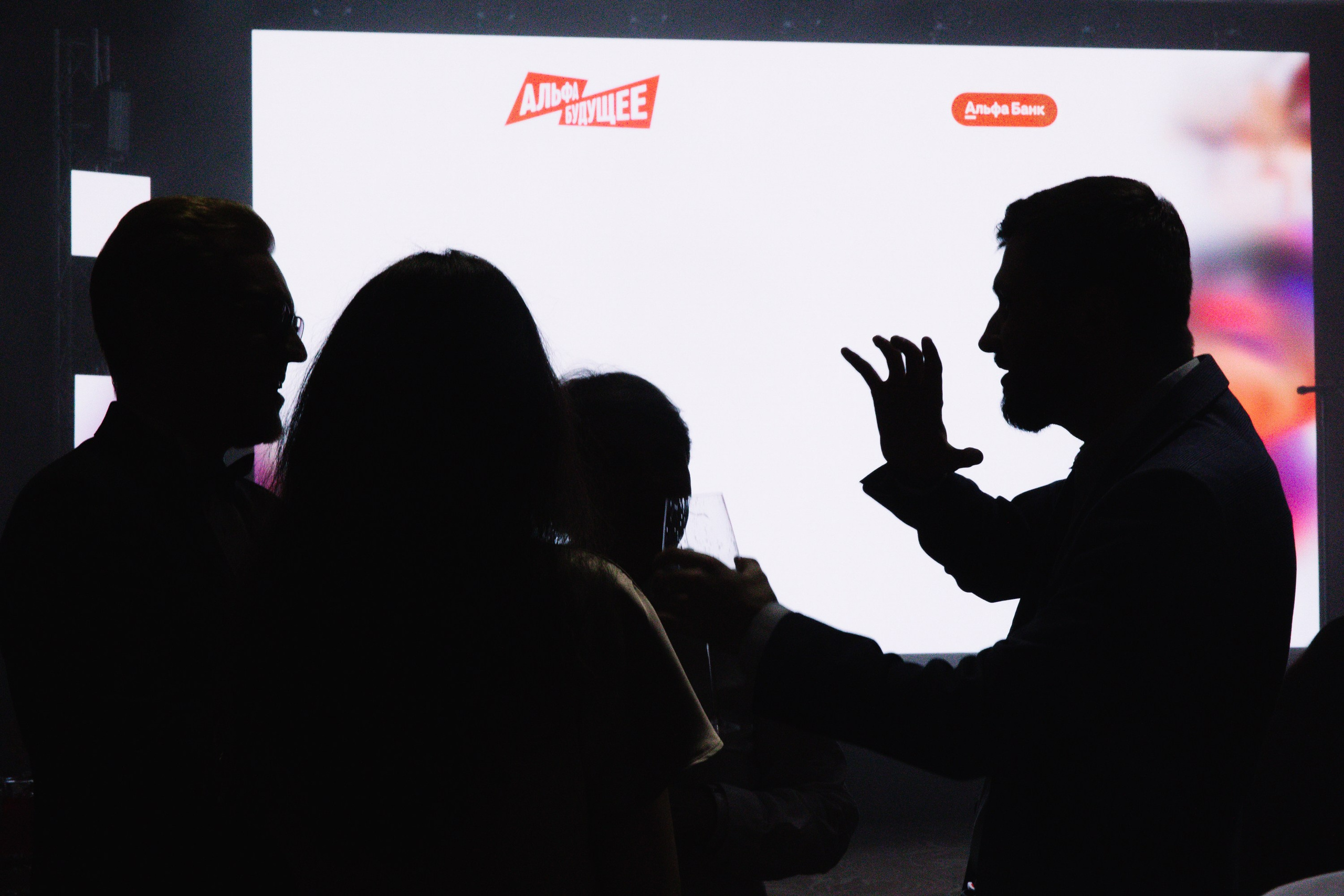 Диалог: Силуэты трех человек на фоне экрана, один из которых активно жестикулирует, рассказывая историю.