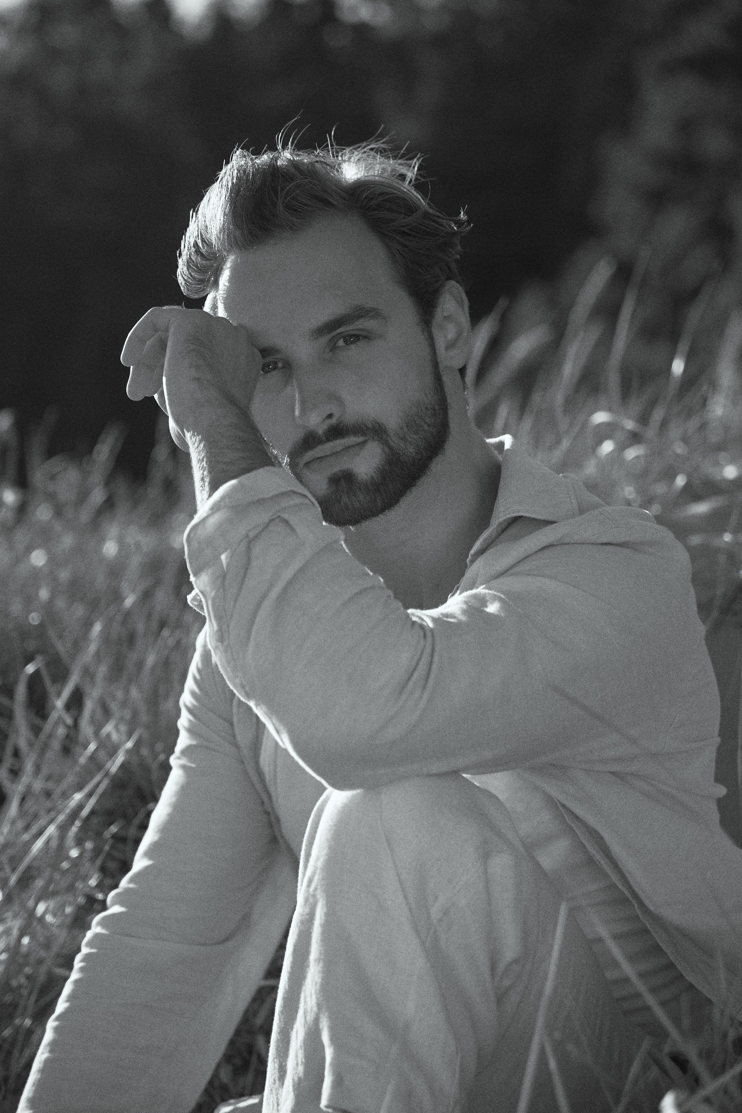 Парень с бородой сидит в поле в траве