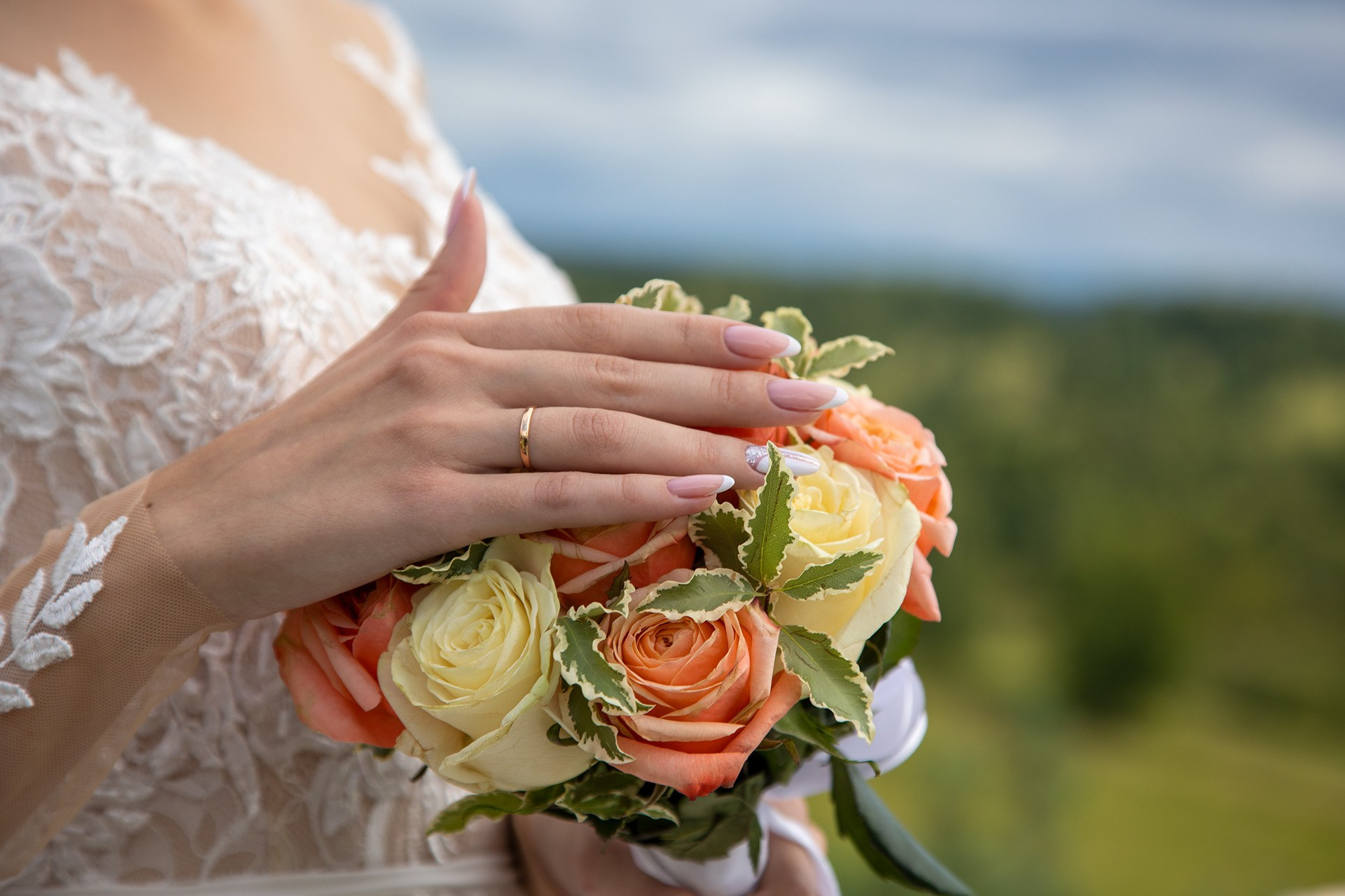 Рука с кольцом невесты на фоне природы с низу букет цветов