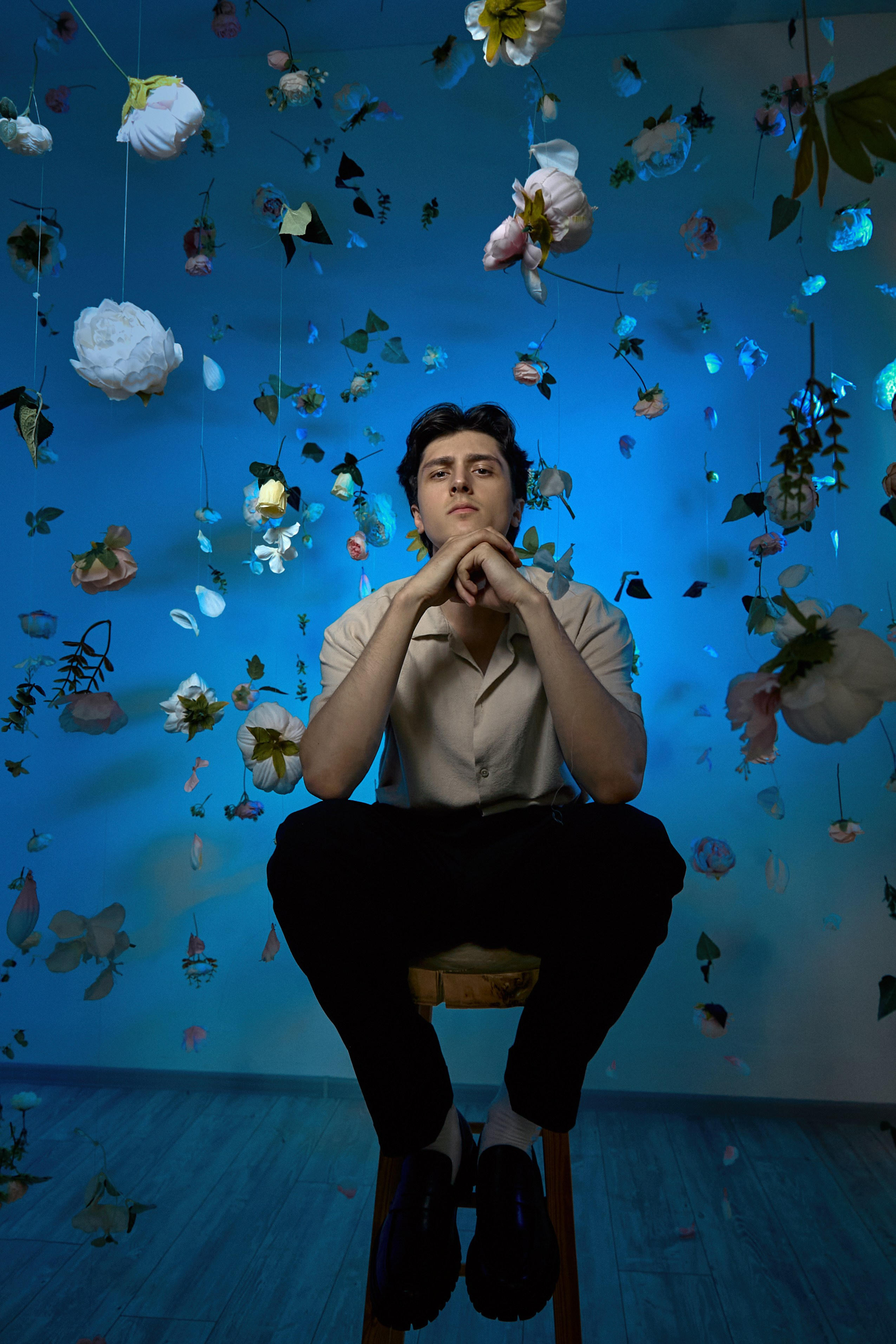 Парень на табурете в парящих цветах с синим светом
