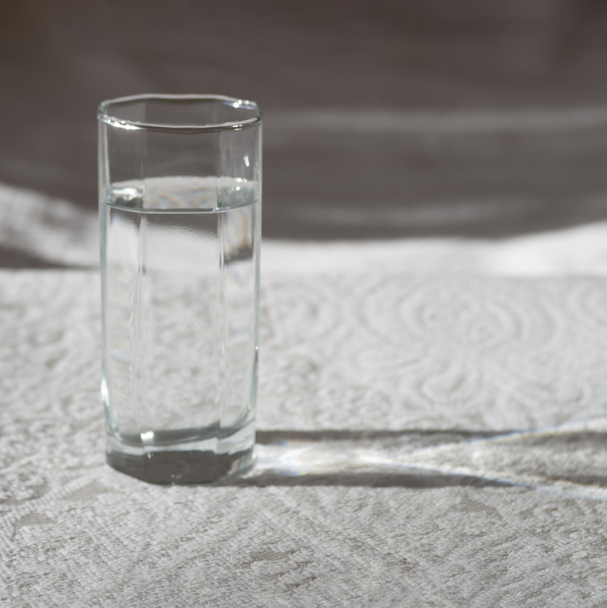 Стакан с водой на скатерти. Яркое боковое освещение.