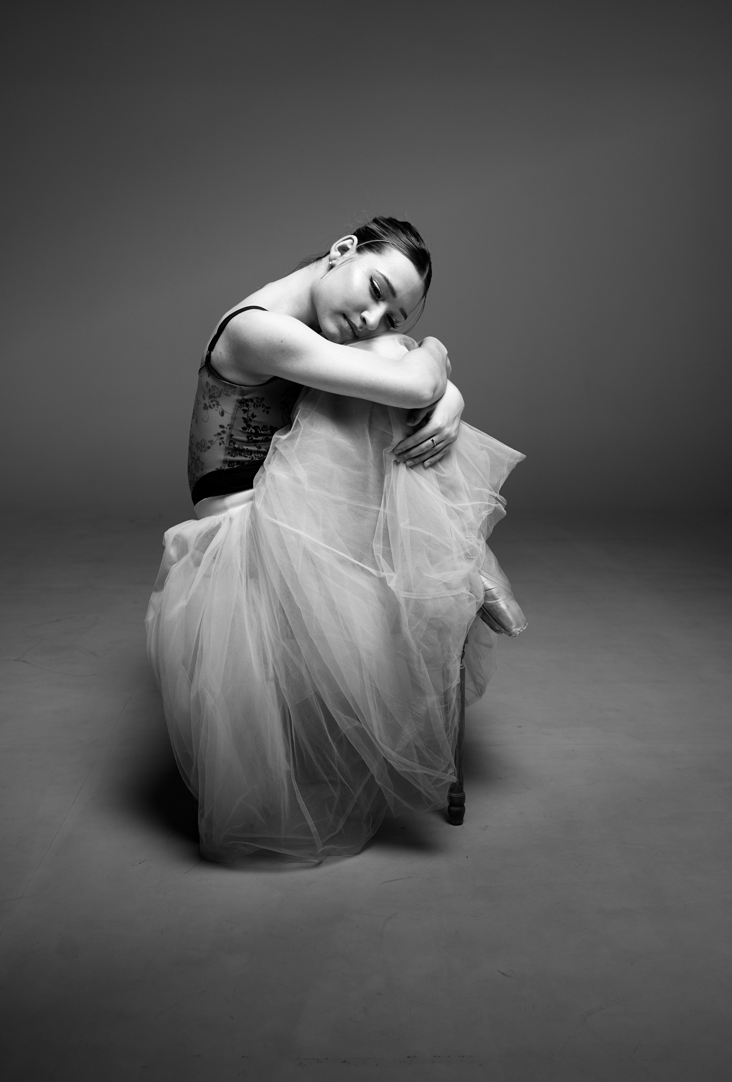 Черно-белый портрет балерины, сидящей на полу и укрытой юбкой - шопенкой. Атмосфера тишины, акцент на текстуре ткани и хрупкости образа. Профессиональное балетное портфолио.