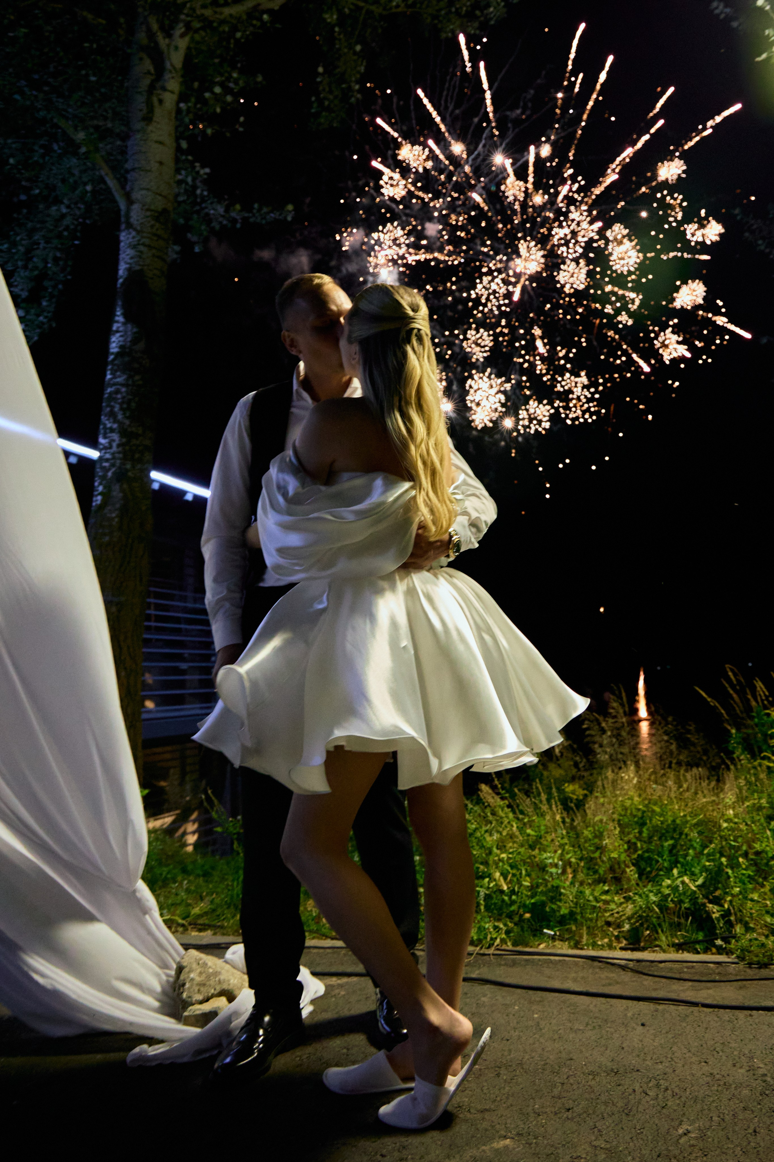 Фотосессия молодых на фоне салюта. Нежный поцелуй жениха и невесты.