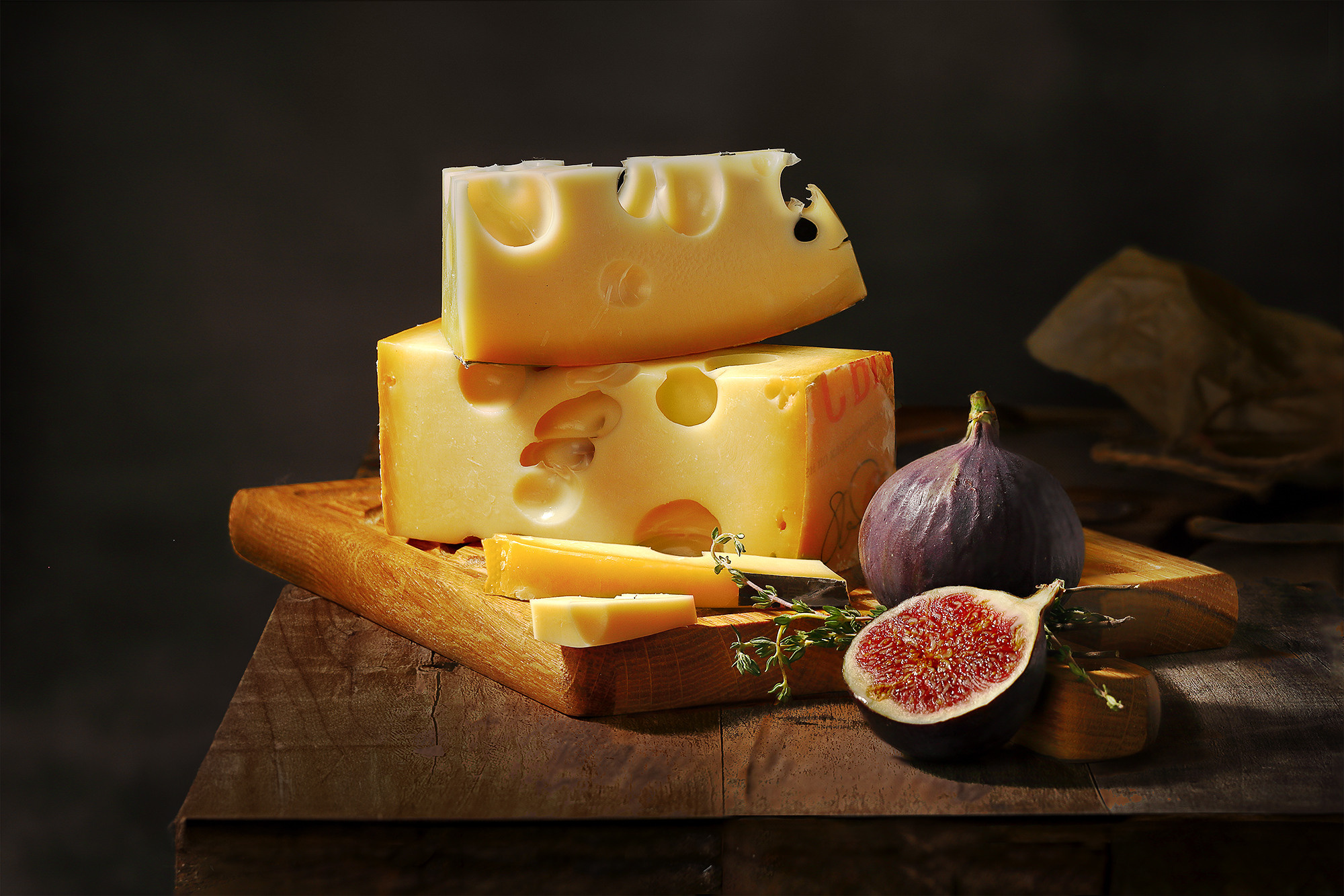 маасдам на деревянной доске в композиции с инжиром на темном фоне, атмосферное фото для рекламы производителя сыра