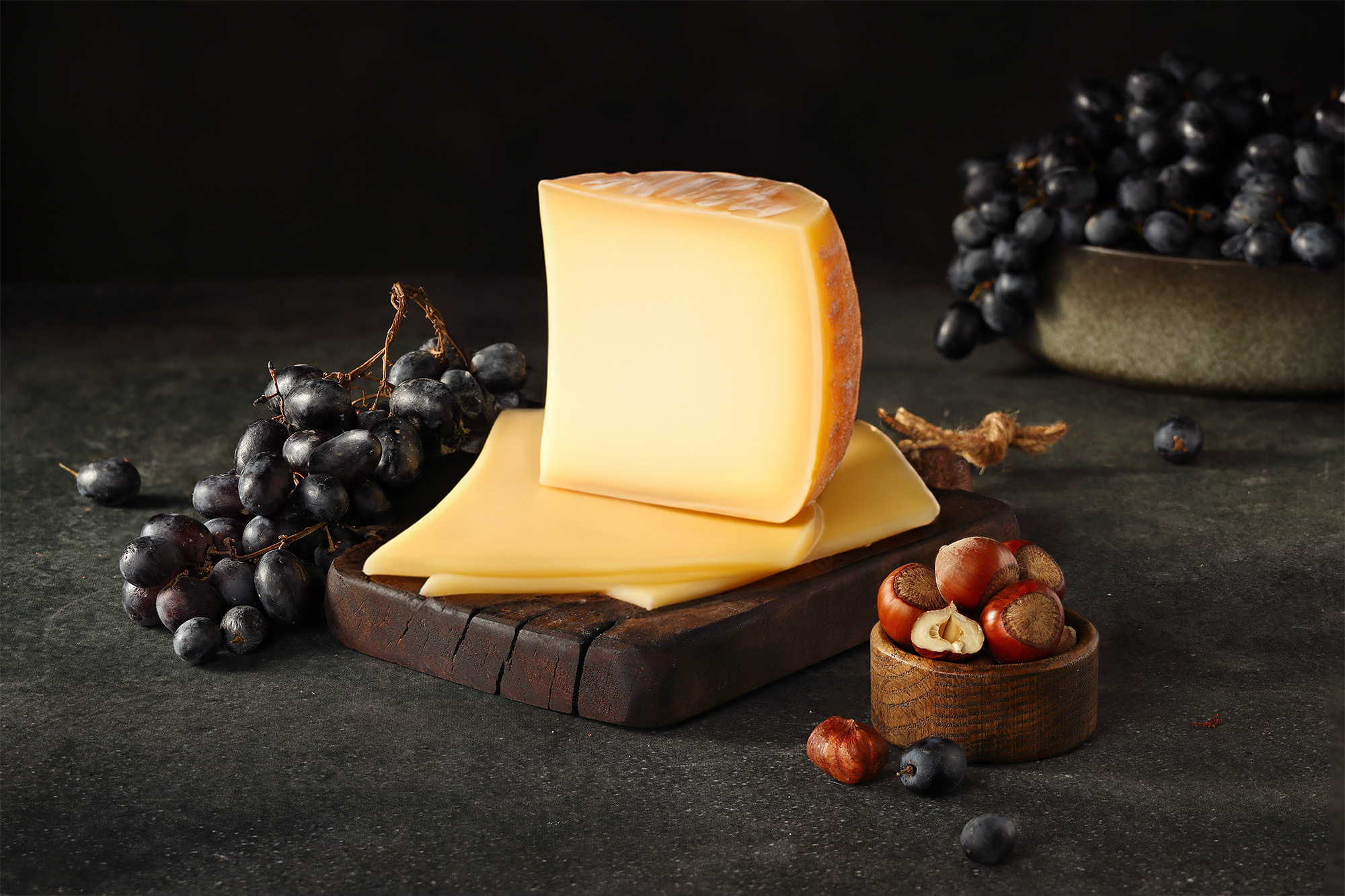 полутвердый сыр с виноградом и фундуком на темном фоне, атмосферное фуд-фото для сыроварни
