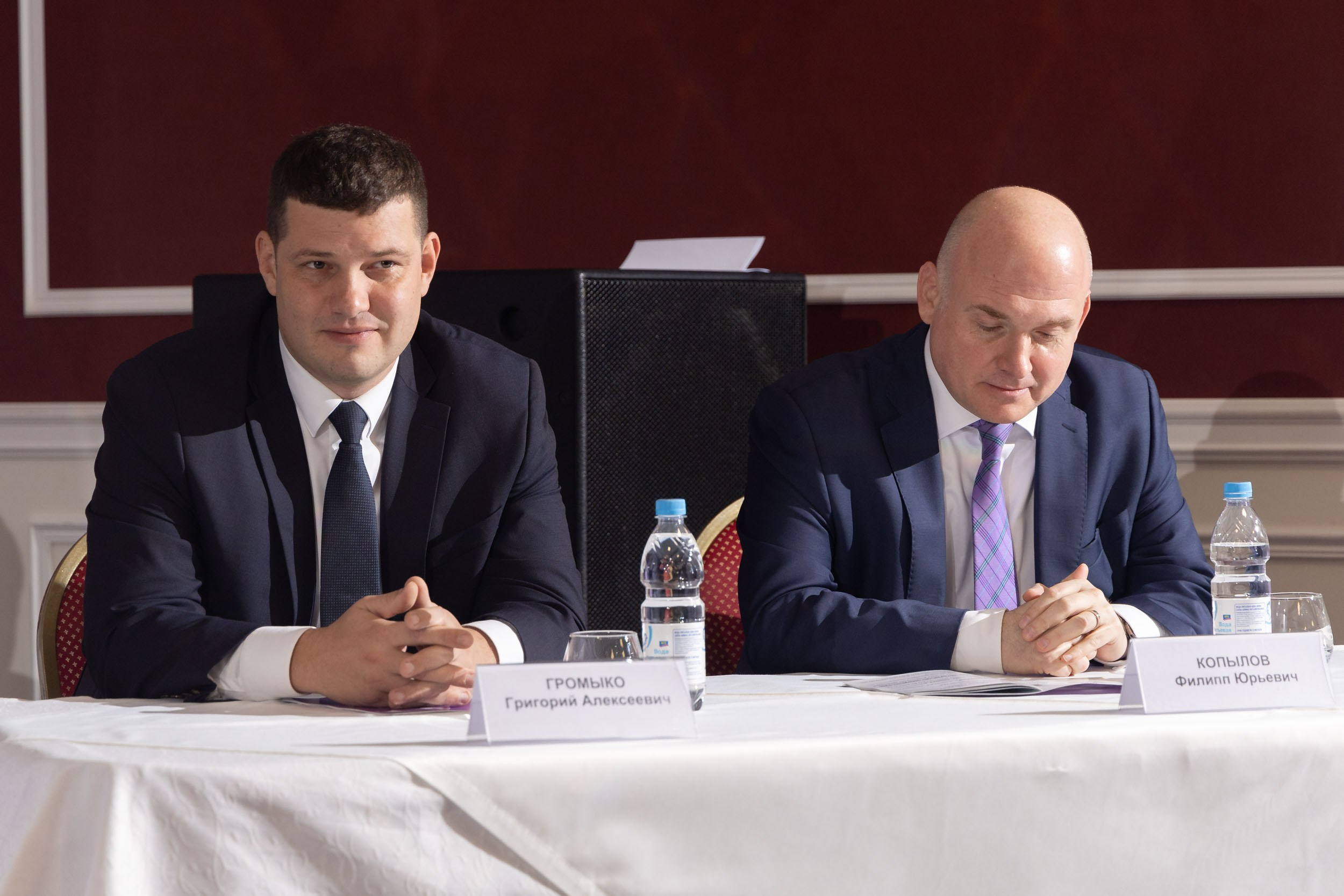 Два мужчины сидят в президиуме за столом с белой скатертью.