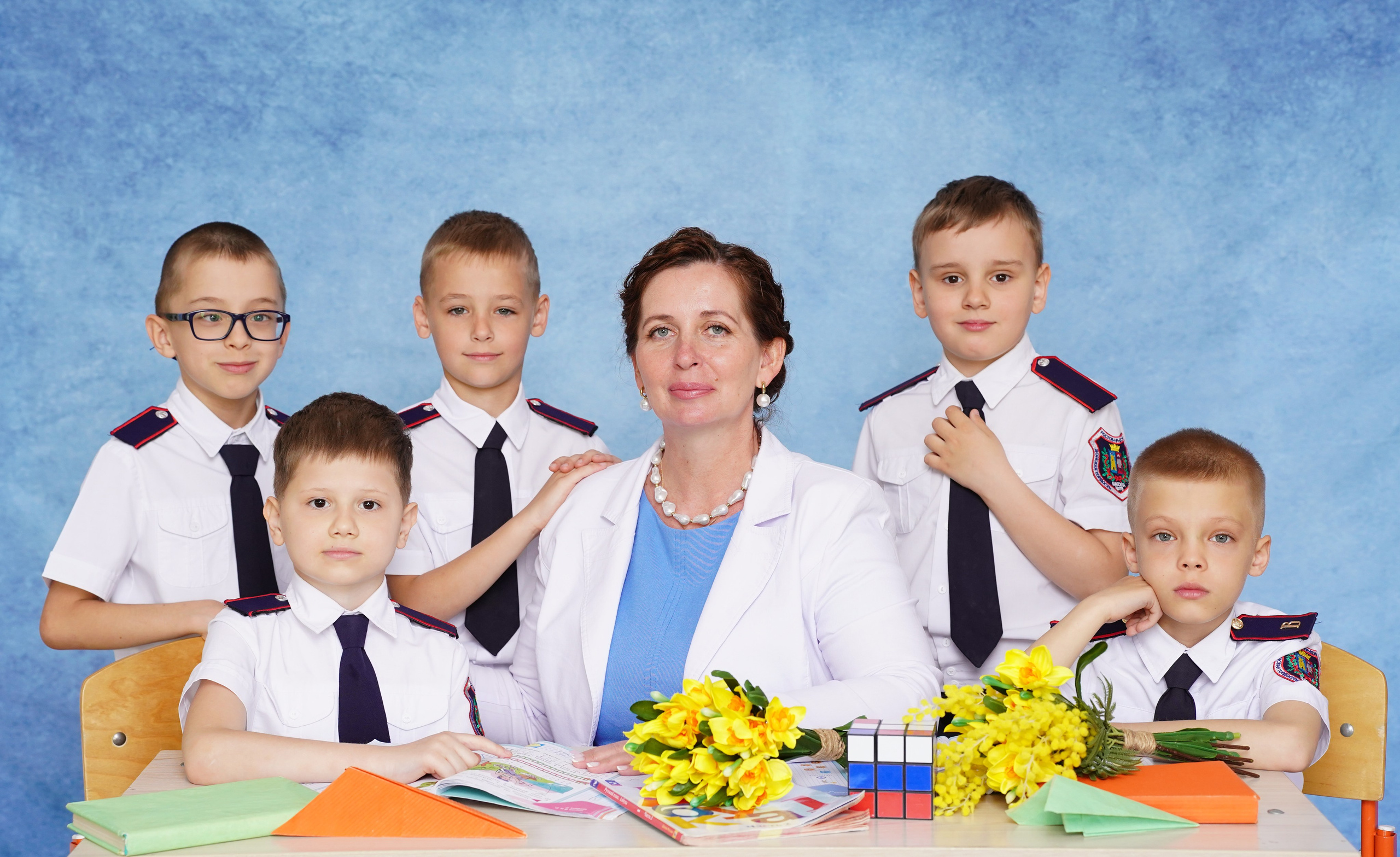 Образец коллективного снимка первоклассников с учителем и друзьями на голубом однотонном фоне.