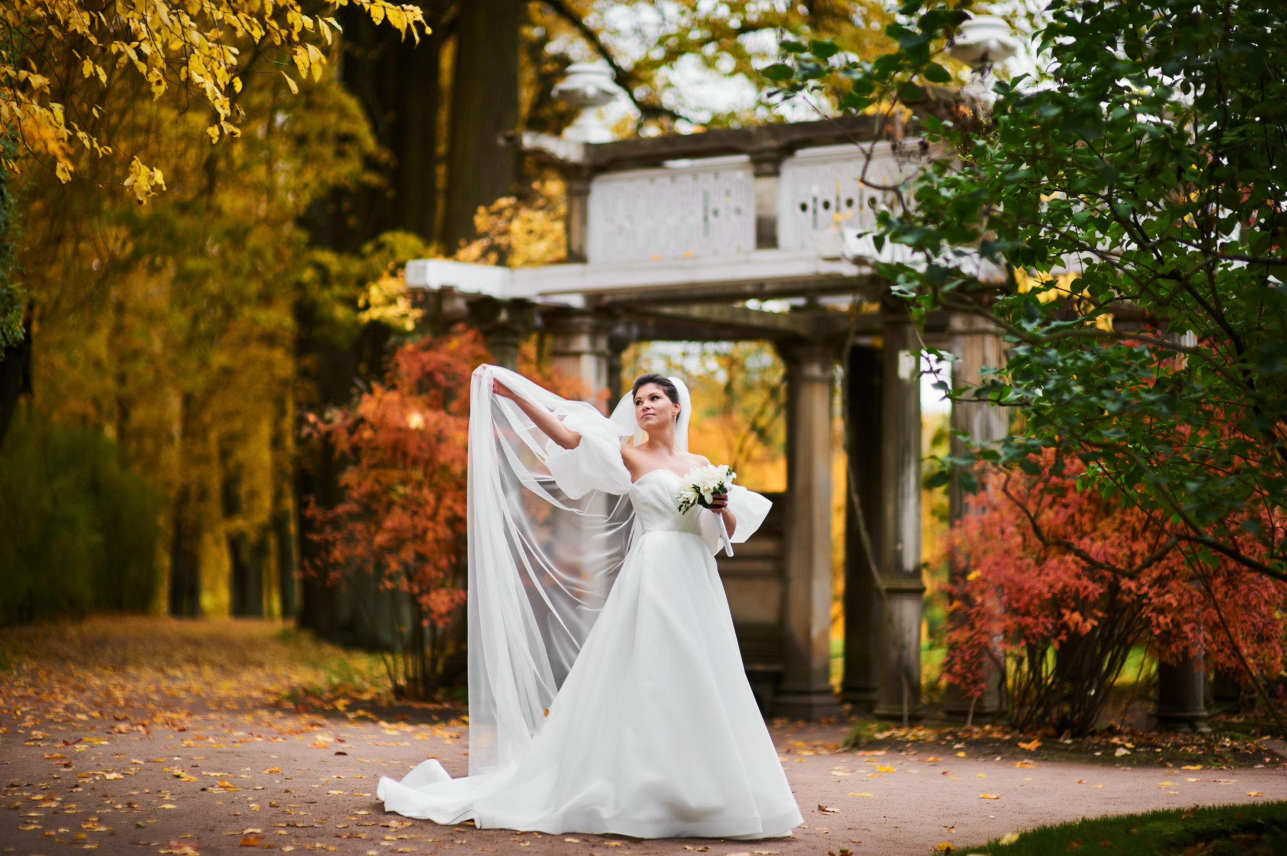 Изящная невеста подкидывает длинную фату на фоне Итальянской беседки в Екатерининском парке осенью в Пушкине