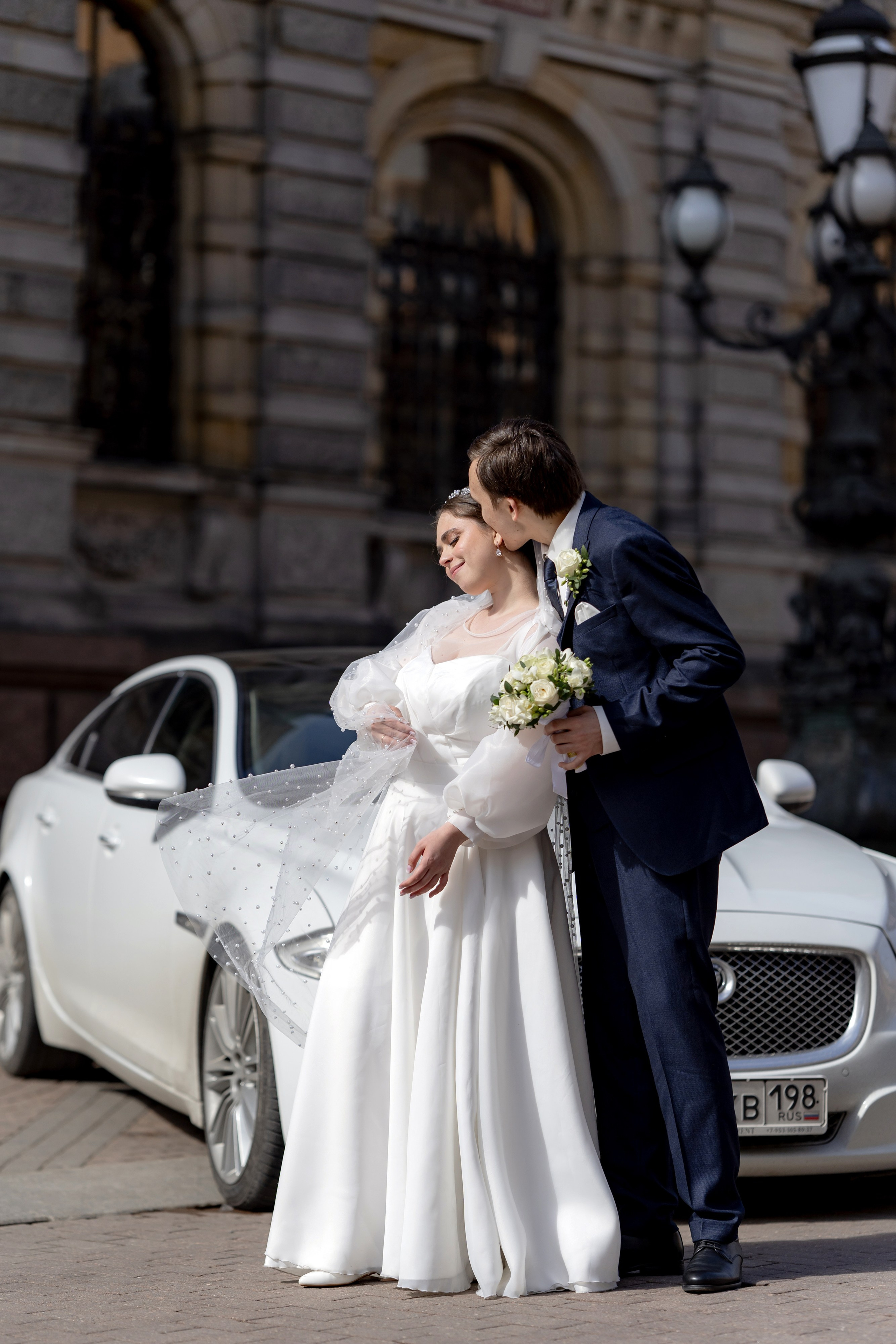 Свадебная фотосессия у Академии Штиглица с автомобилем. Жених красиво целует невесту у автомобиля ягуар