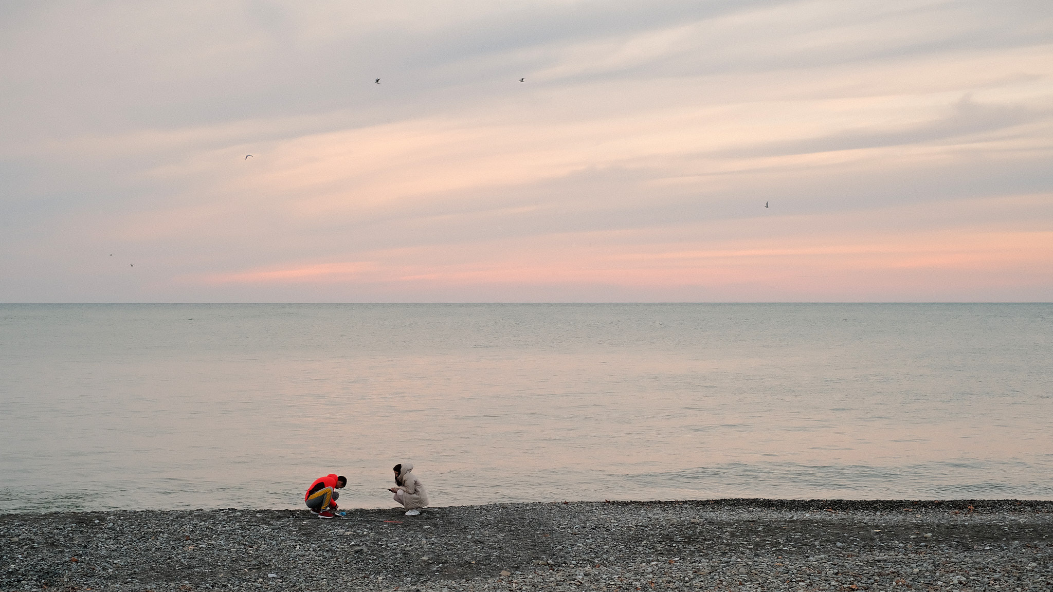 Sunset. The mouth of the Sochinka river. Sea view. The fisherman changes the bait on the fishing rod. Seagulls form an arch against the background of the sunset sky. (Закат. Устье реки Сочинки. Вид на море. Рыбак меняет наживку на удочке. Чайки на фоне закатного неба образуют арку.)