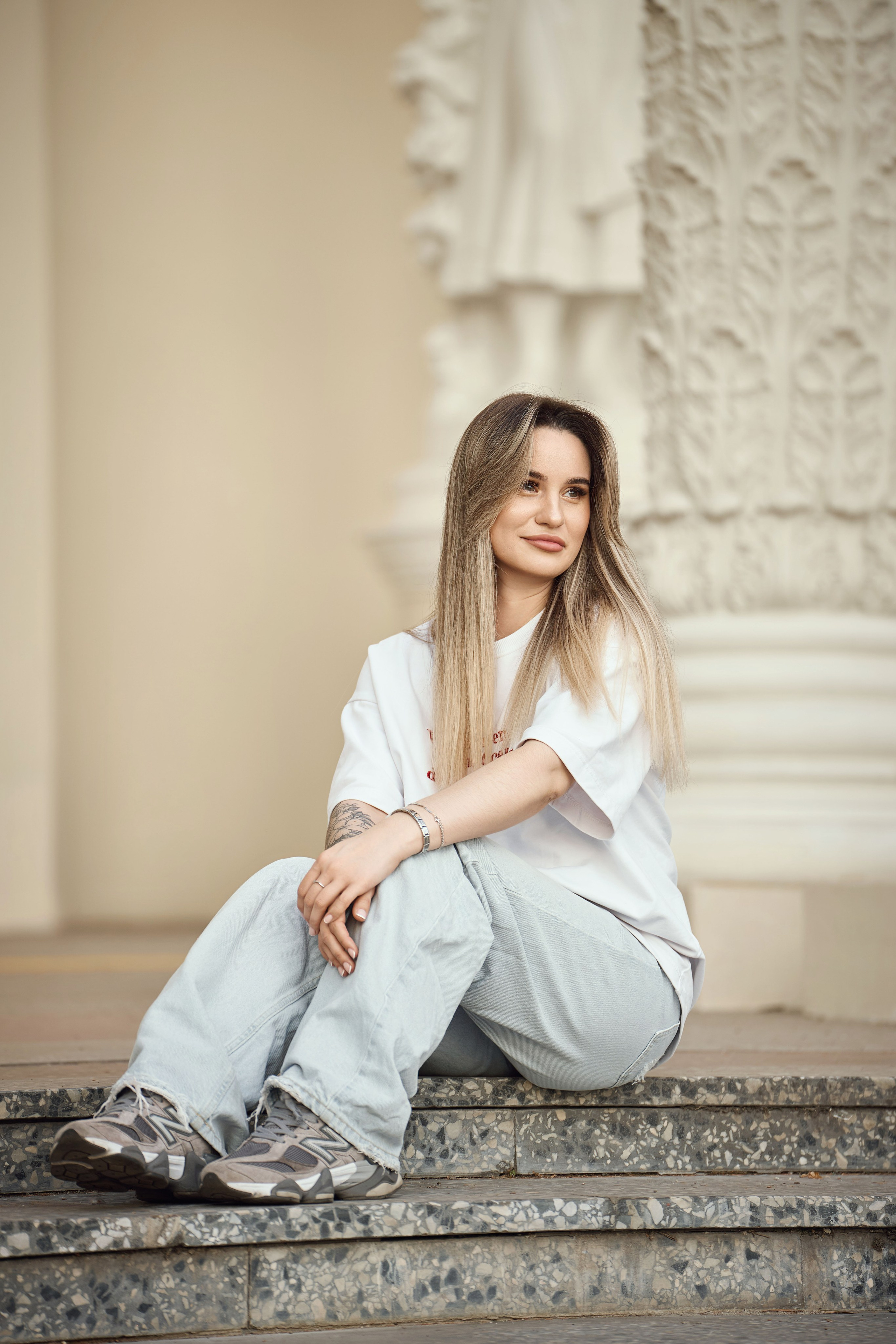 девушка в белой рубашке и синих джинсах сидит на ступенях павильона ВДНХ