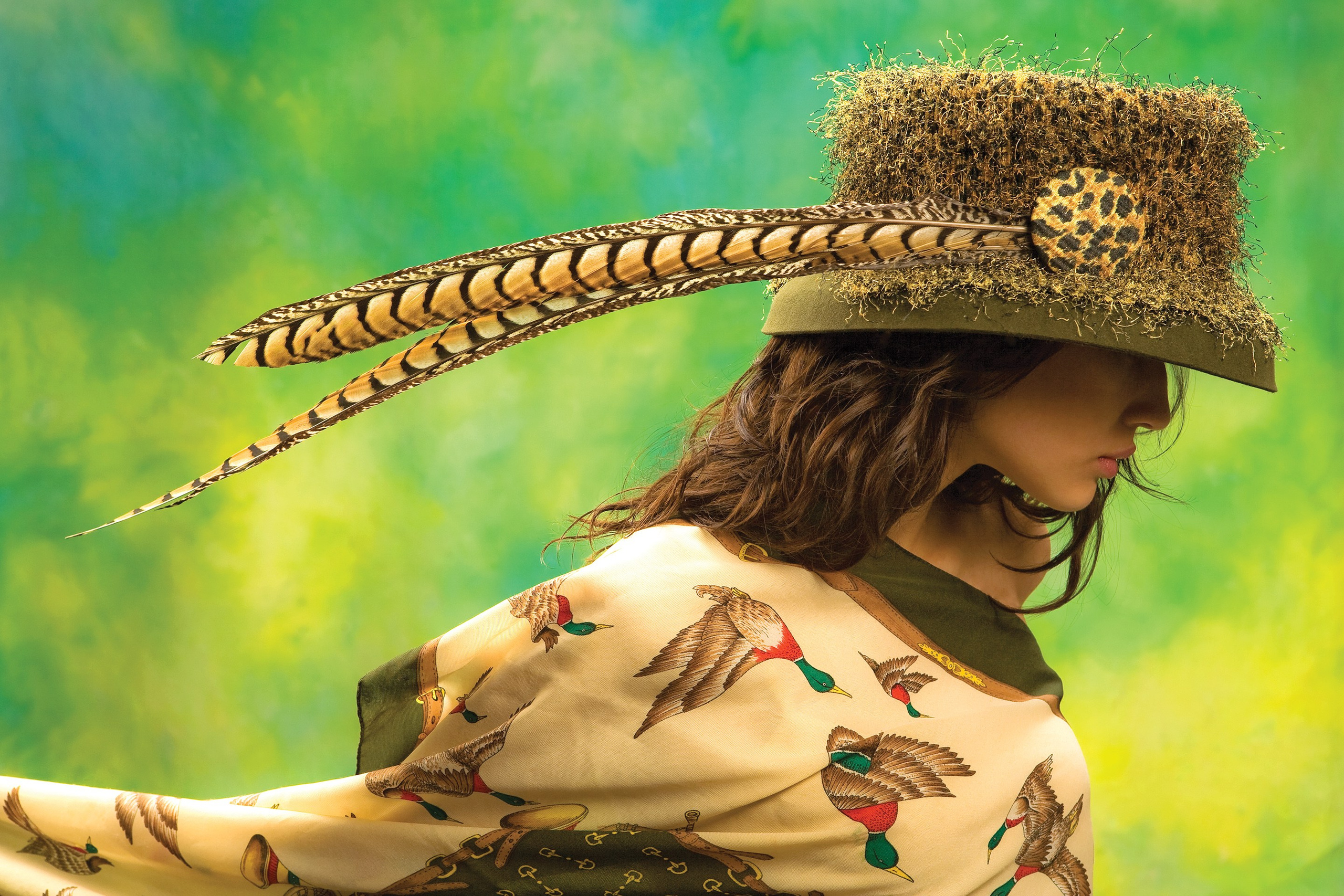 Студийная фотосъёмка девушки в шляпе с пером в охотничьем стиле.