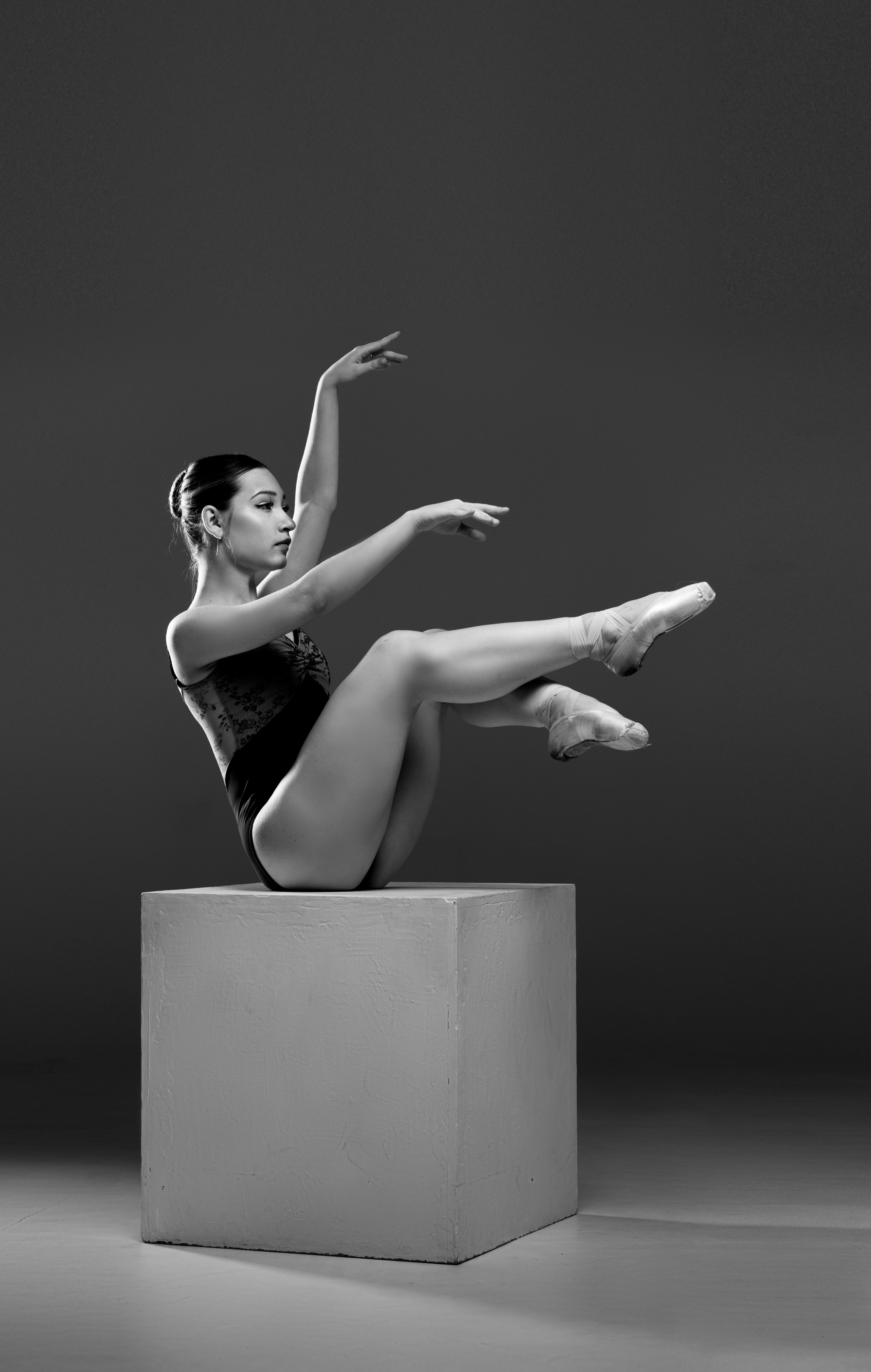 Черно-белый кадр с балериной на белом кубе в динамичной позе. Акцент на графике рук, силе мышц и эстетике современного танца в стиле спорт-арт.