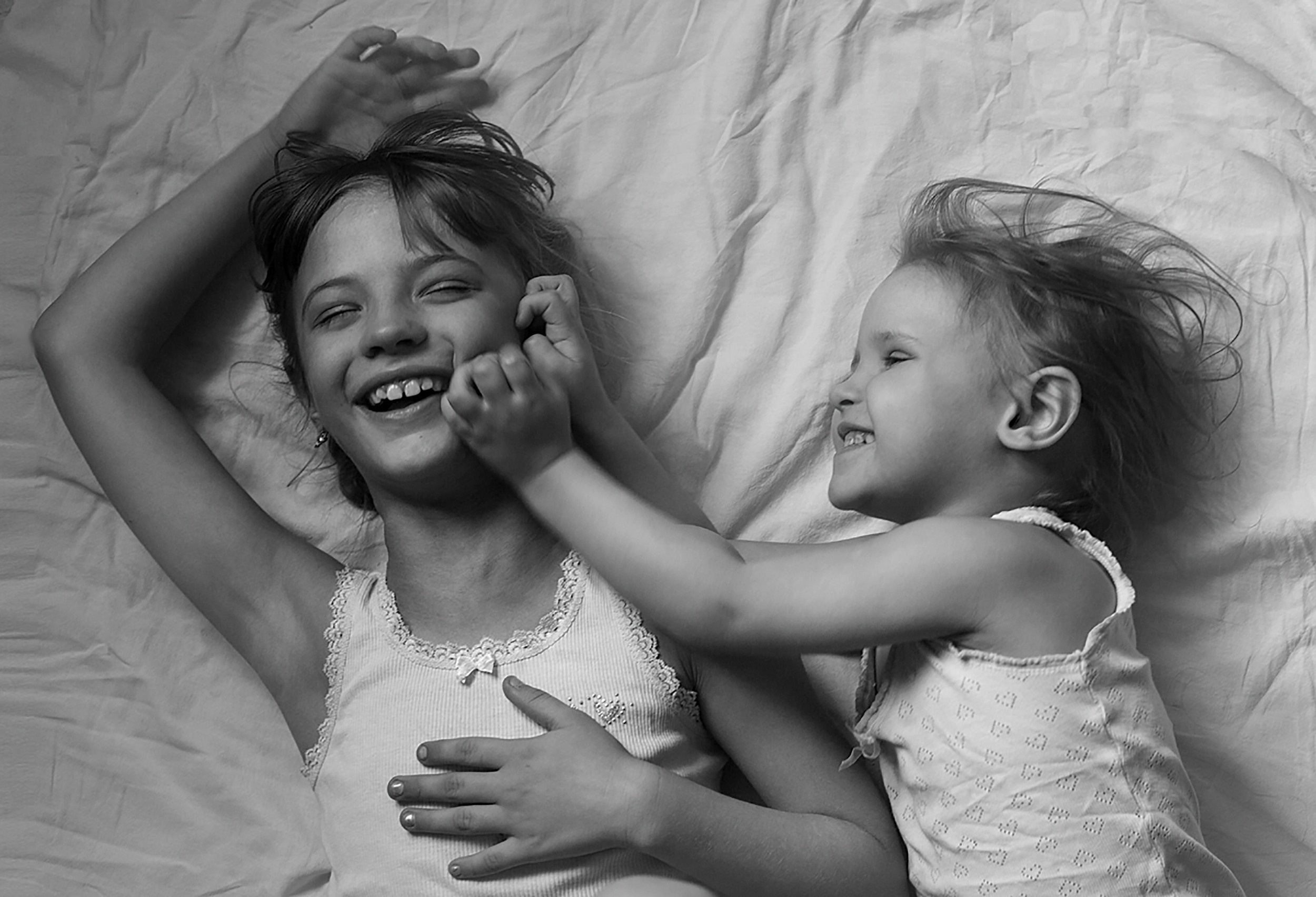 Две сестры резвятся на постели в майках. 