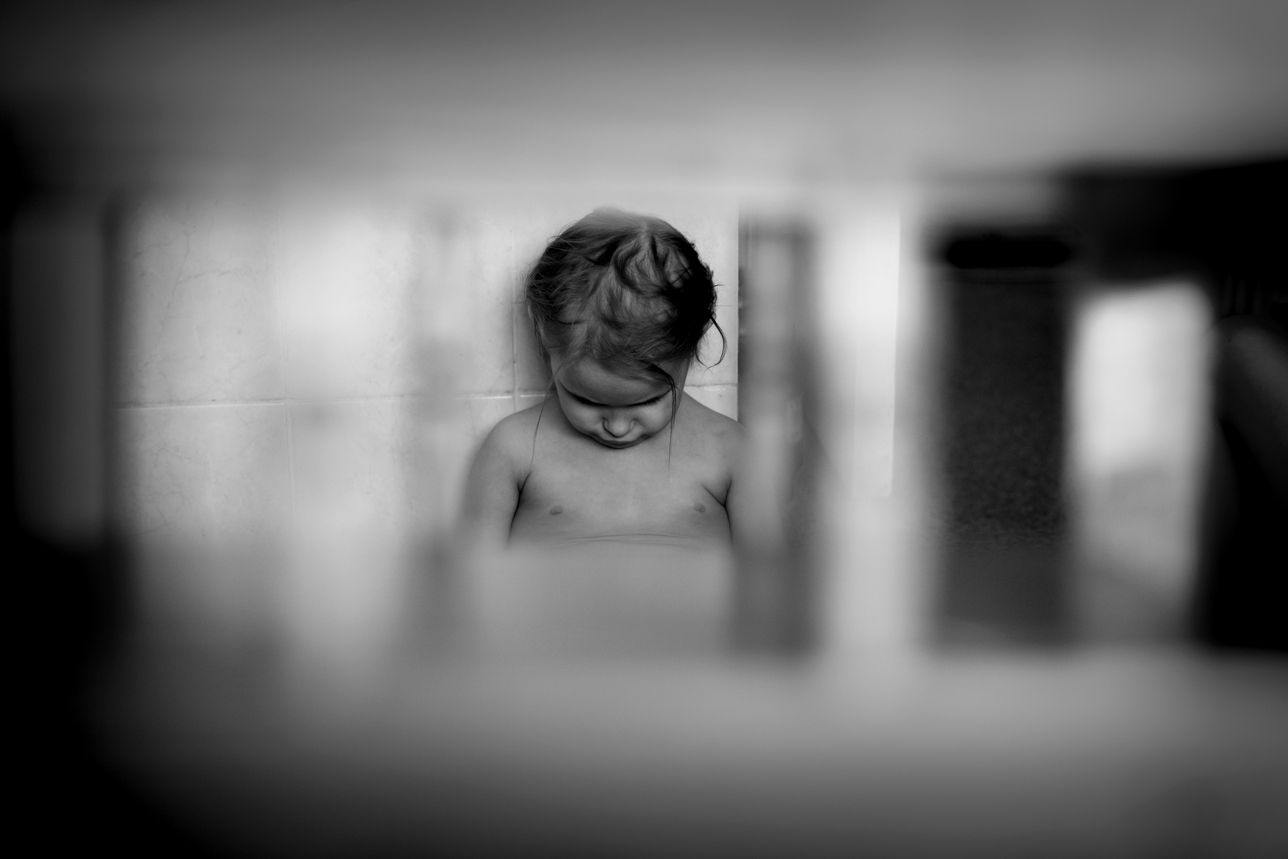 Обидевшаяся девочка грусти и плачет в кухне, склонив голову к коленям.