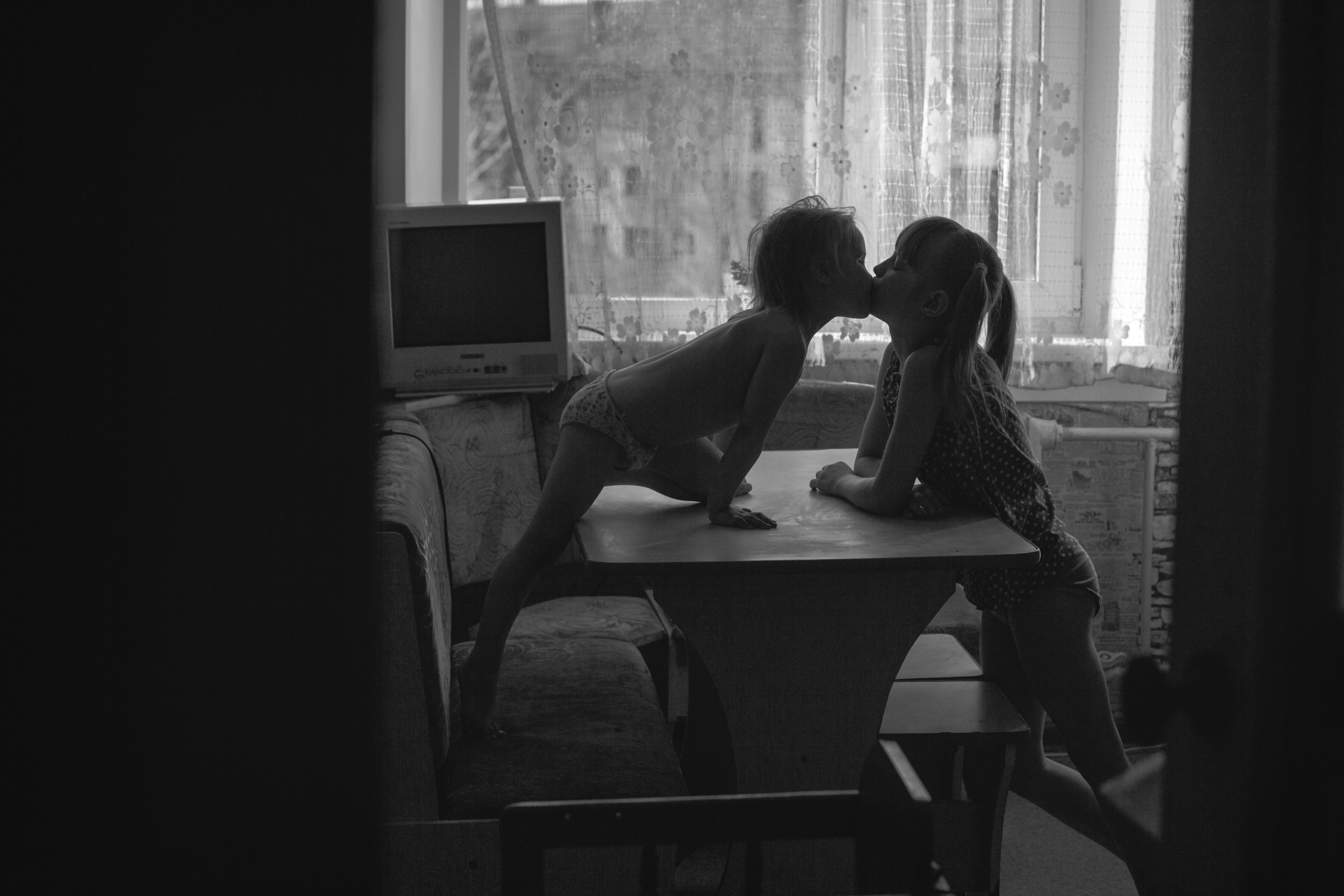 Две сестры целуются после обеда на кухне за столом.