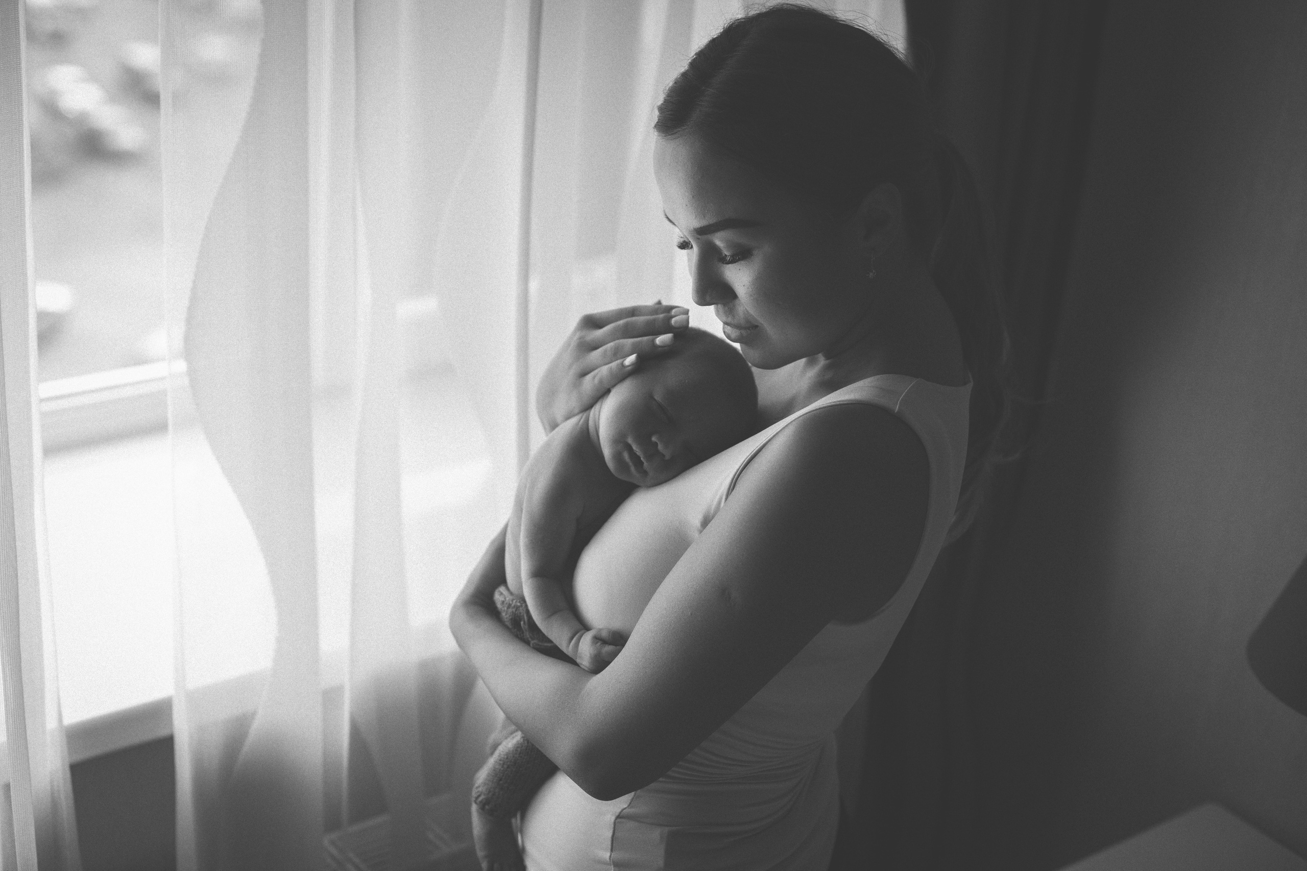 мама с новорождённым на руках у окна.