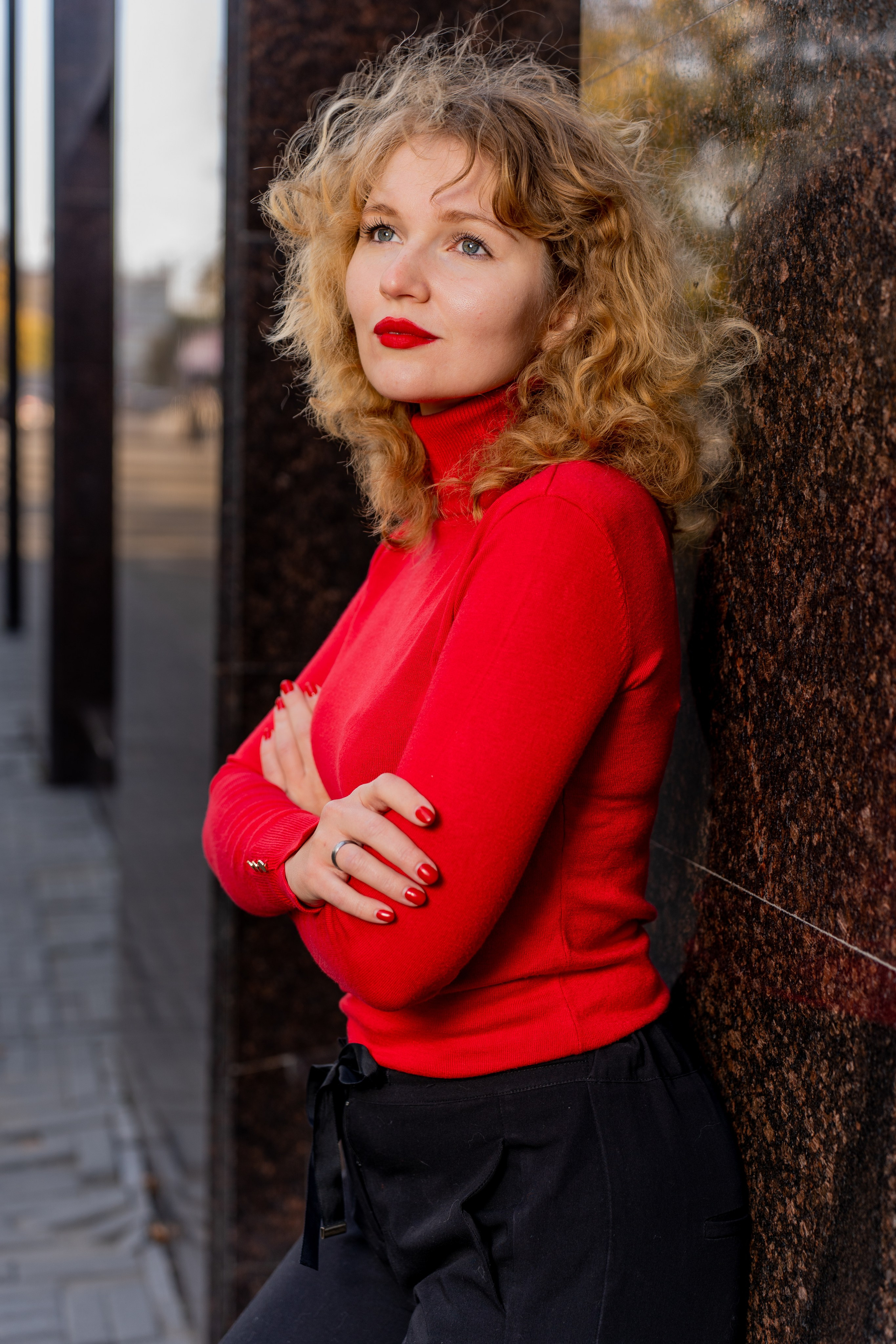 Портрет модели в красном свитере на фоне городской архитектуры