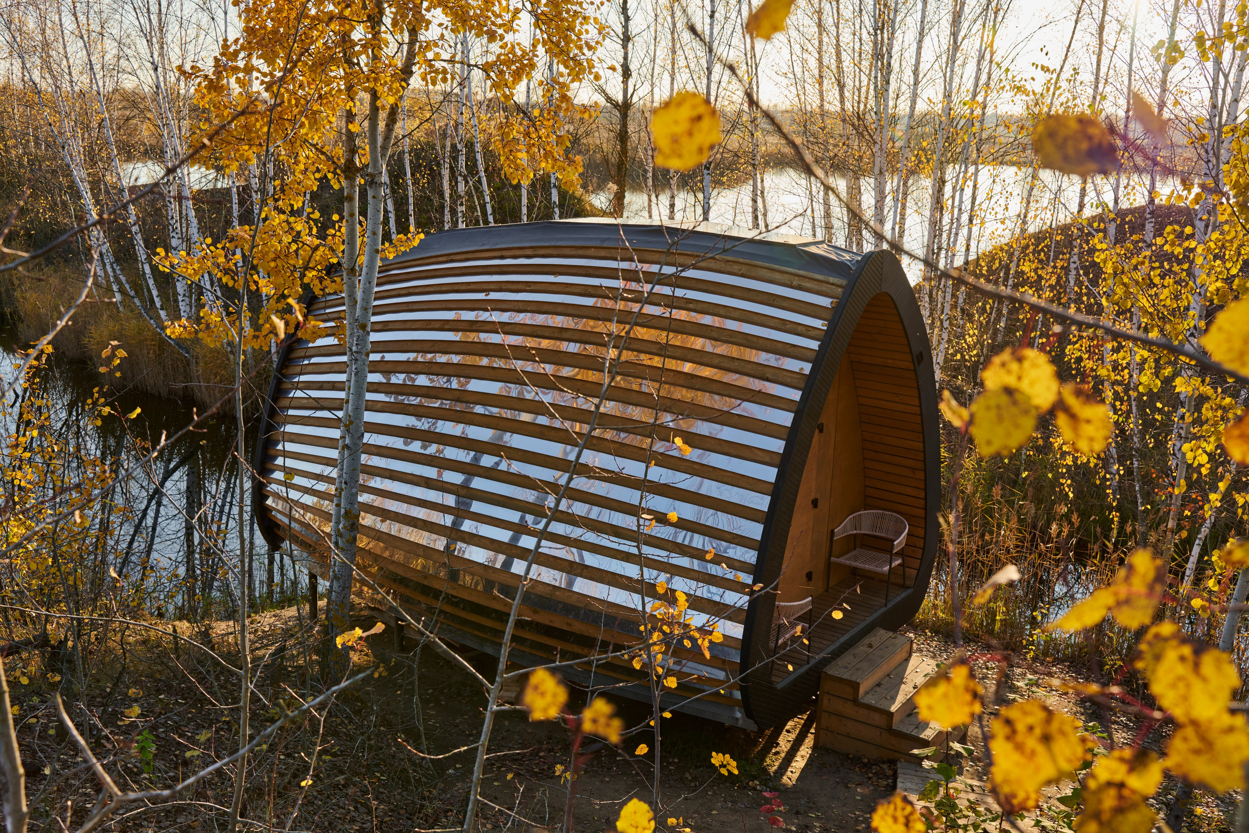 Скамья-качели на берегу, листья и вода рядом.