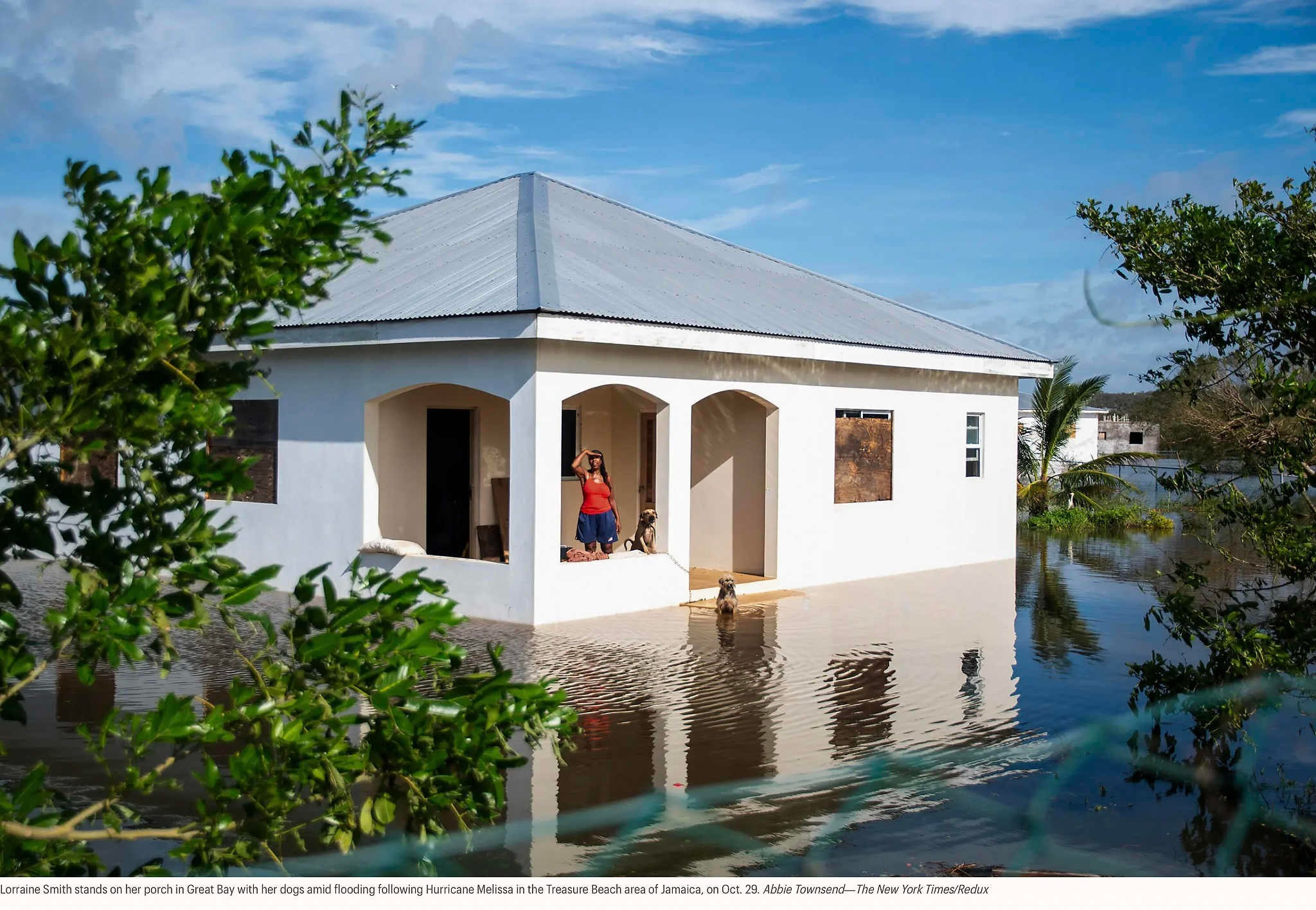 Лоррейн Смит стоит на крыльце своего дома в Грейт-Бэй со своими собаками во время наводнения, вызванного ураганом «Мелисса» в районе Трежер-Бич на Ямайке, 29 октября. Эбби Таунсенд — The New York Times/Redux