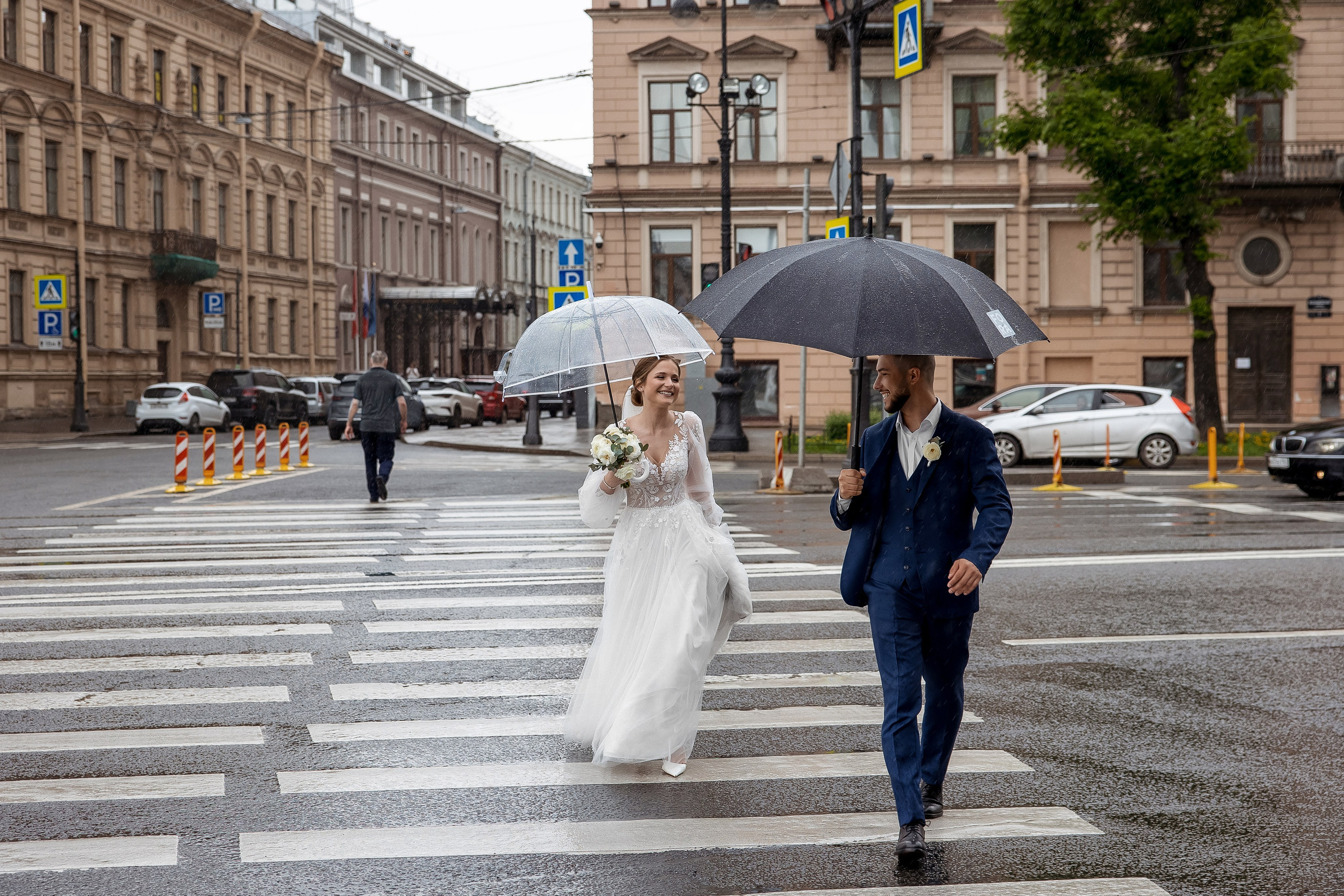 Жених и невеста перебегают дорогу по пешеходному переходу во время дождя