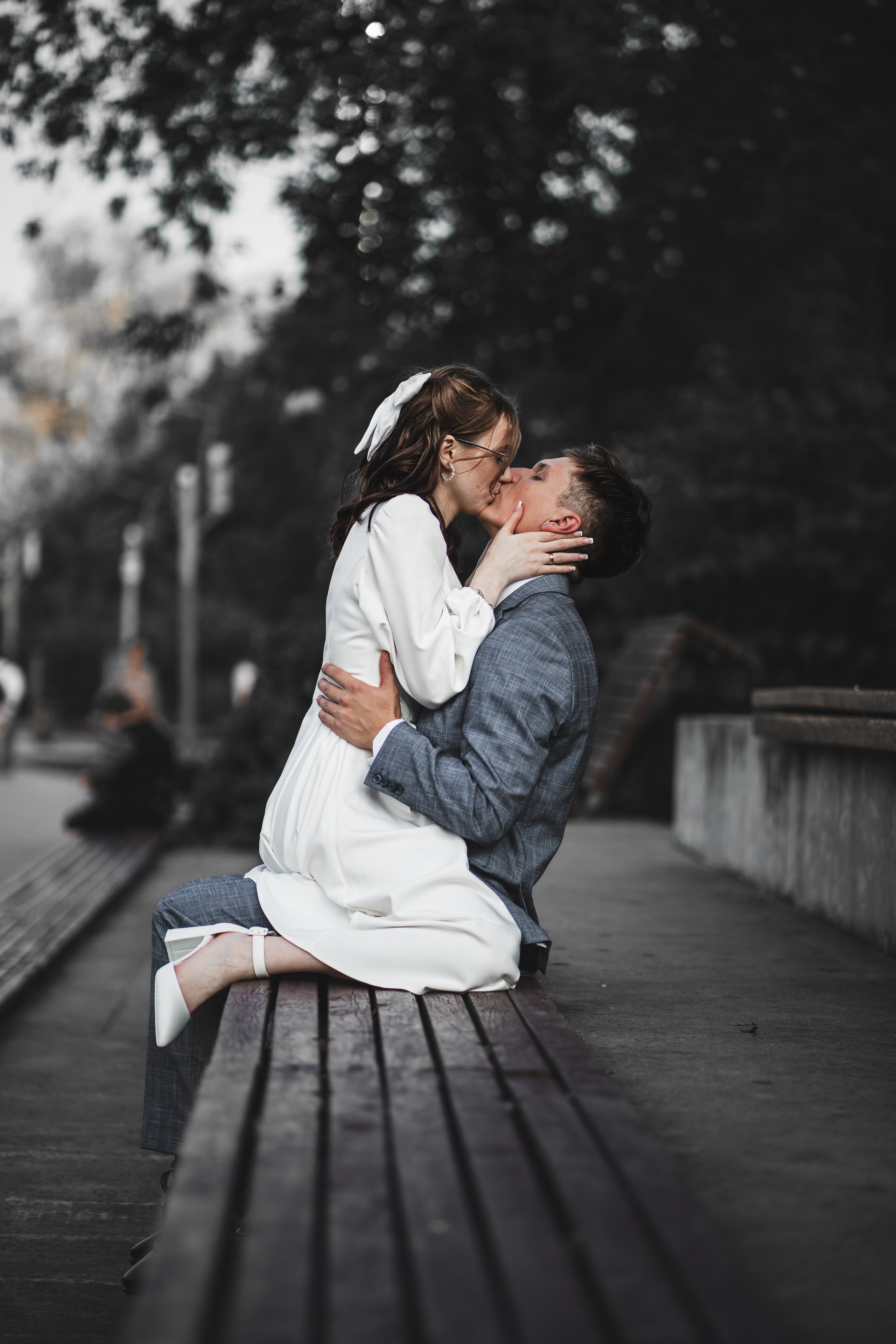 Молодожены целуются на скамейке в парке