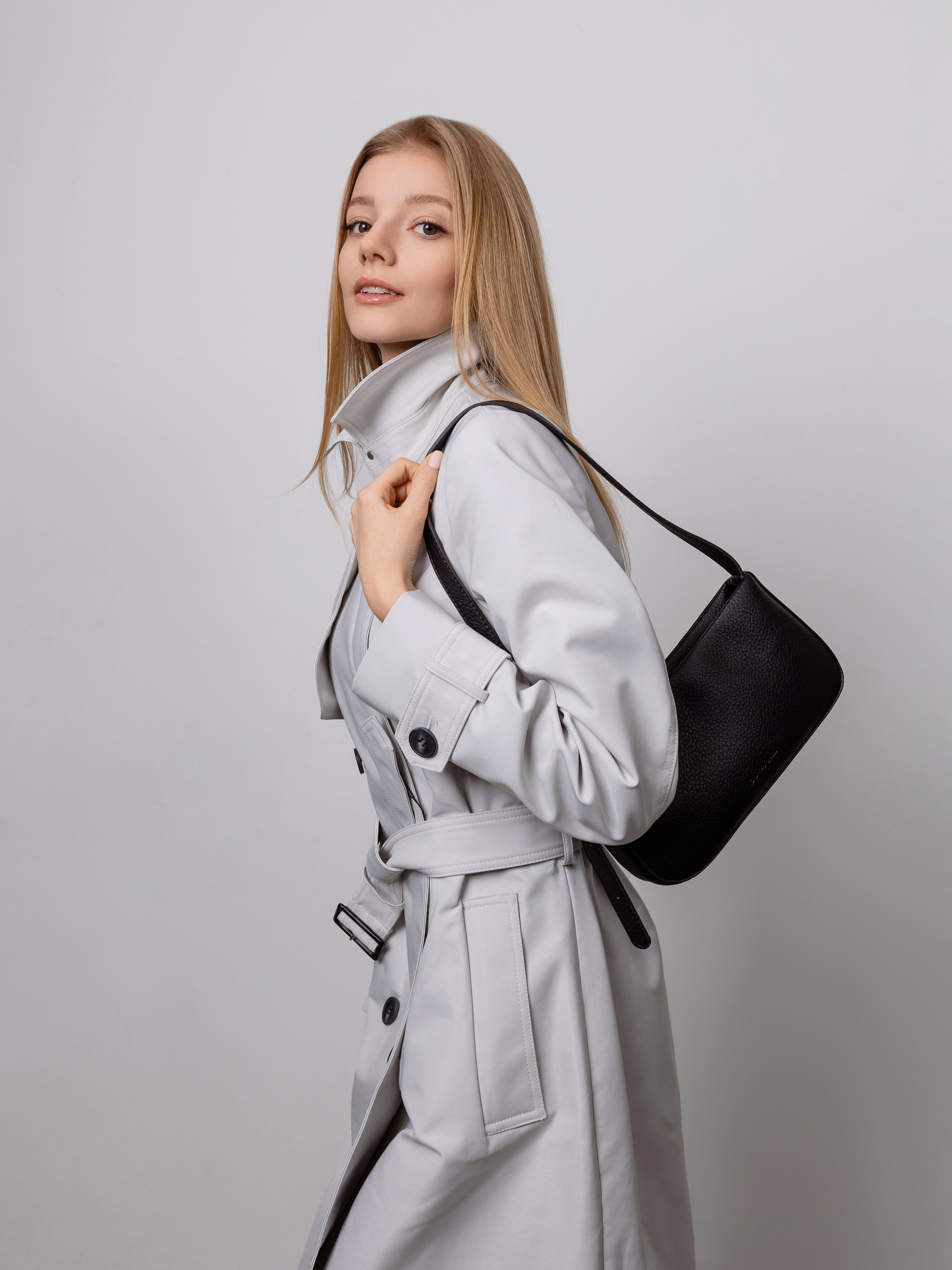 У девушке в белом плаще черная сумочка накинута на левое плечо.