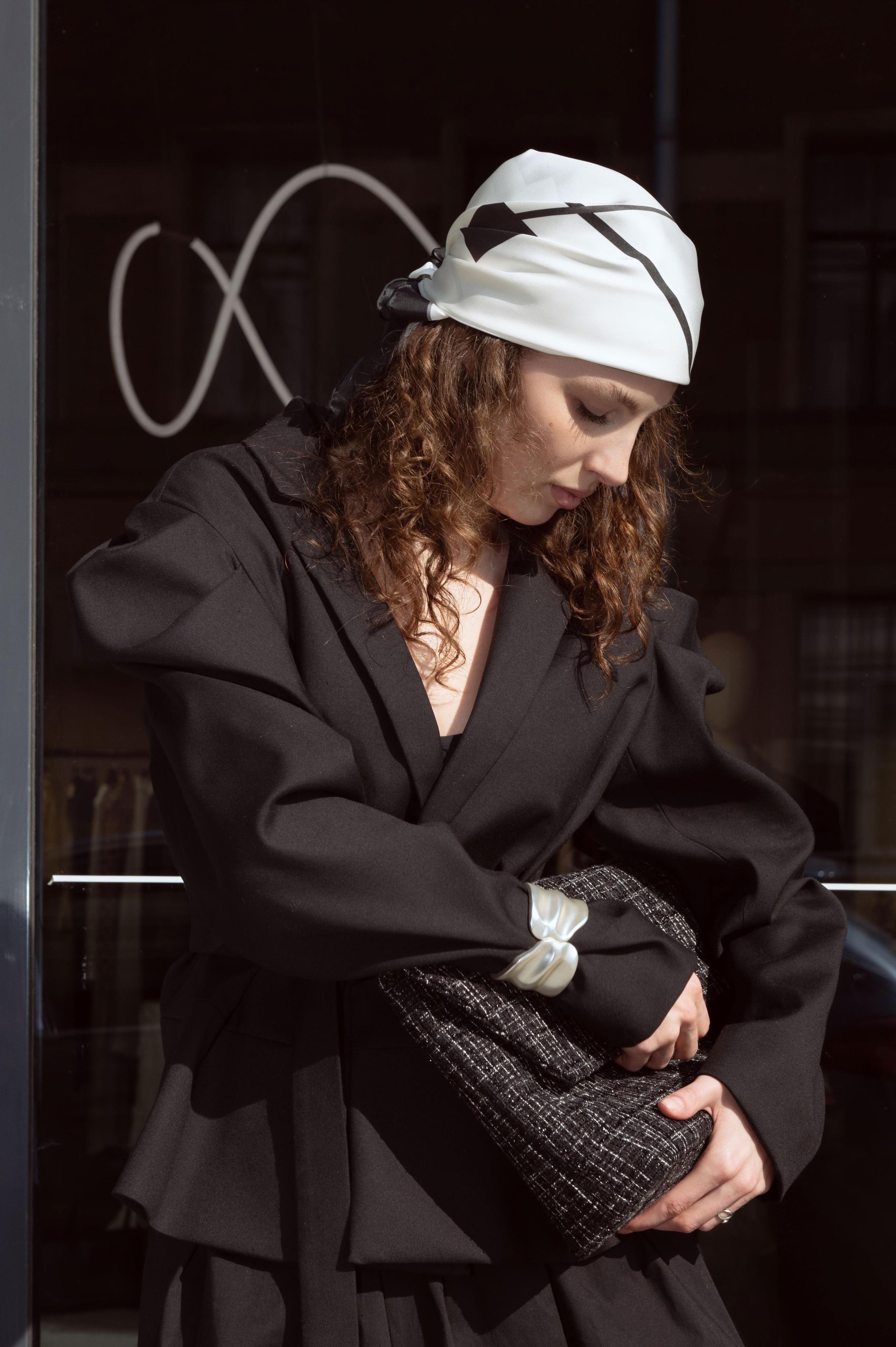 Красивая девушка в дизайнерской одежде и шелковом дизайнерском платке стоит на фоне витрины бутика