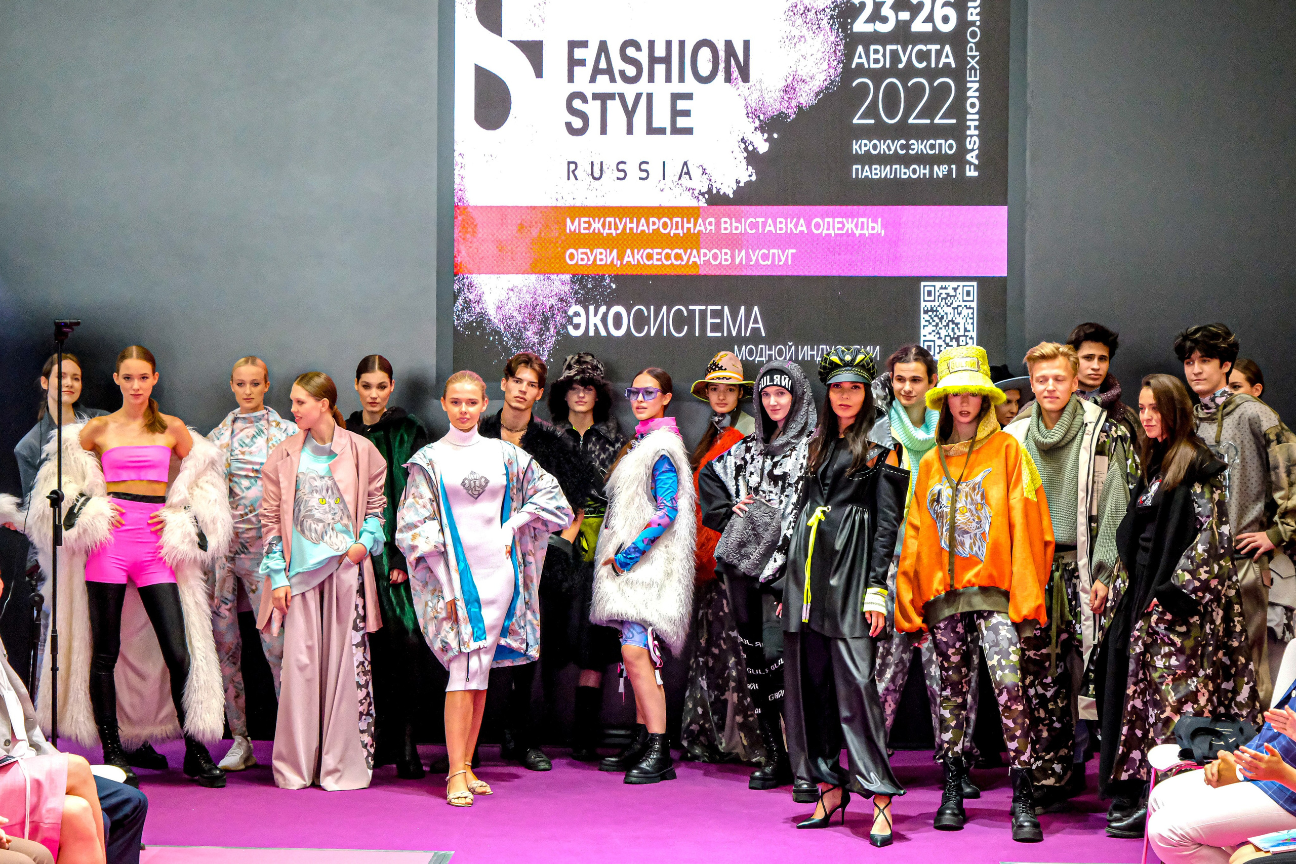  "Модели в ярких нарядах проходят по подиуму во время показа мод, освещенные яркими софитами и окруженные восторженными зрителями."