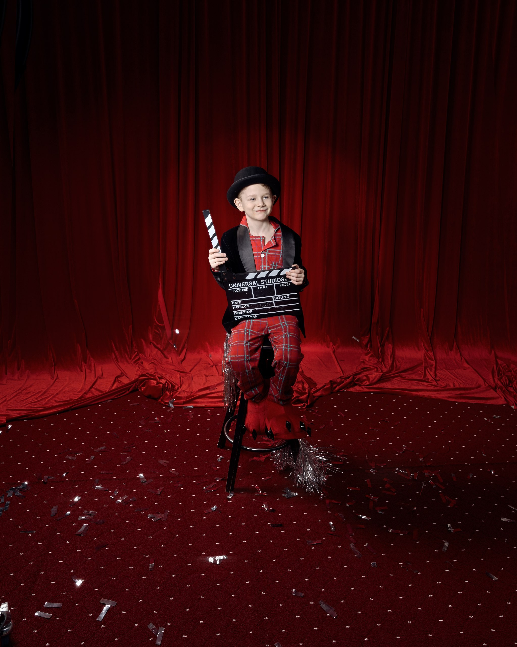 Новогодняя фотосессия в Красноярске.Детская тематическая фотосессия в стиле кино: мальчик в костюме режиссера с хлопушкой на фоне красной занавески. Художественная фотосессия