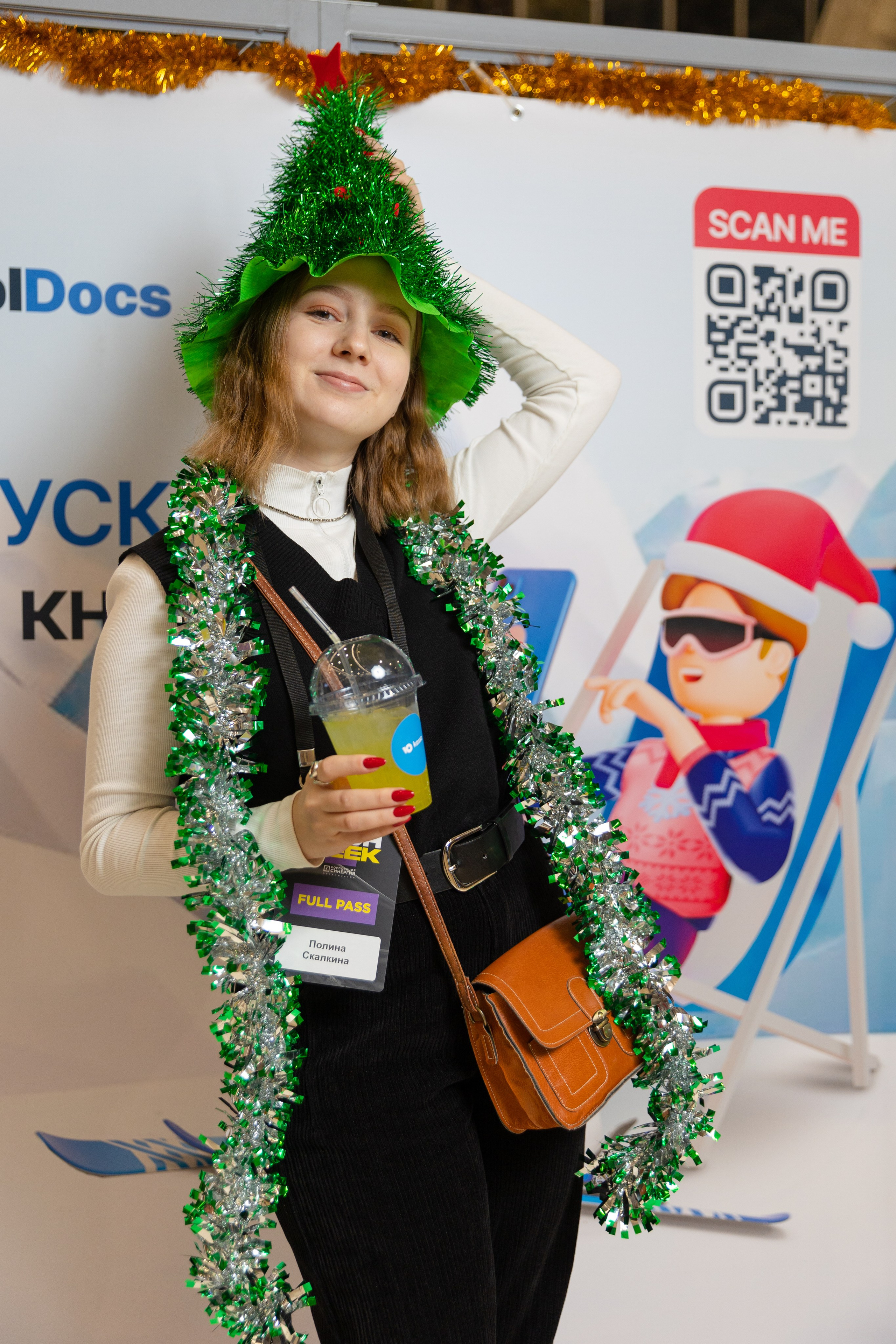 девушка В шапке ёлке и мишуре позирует на фоне баннера  на выставке