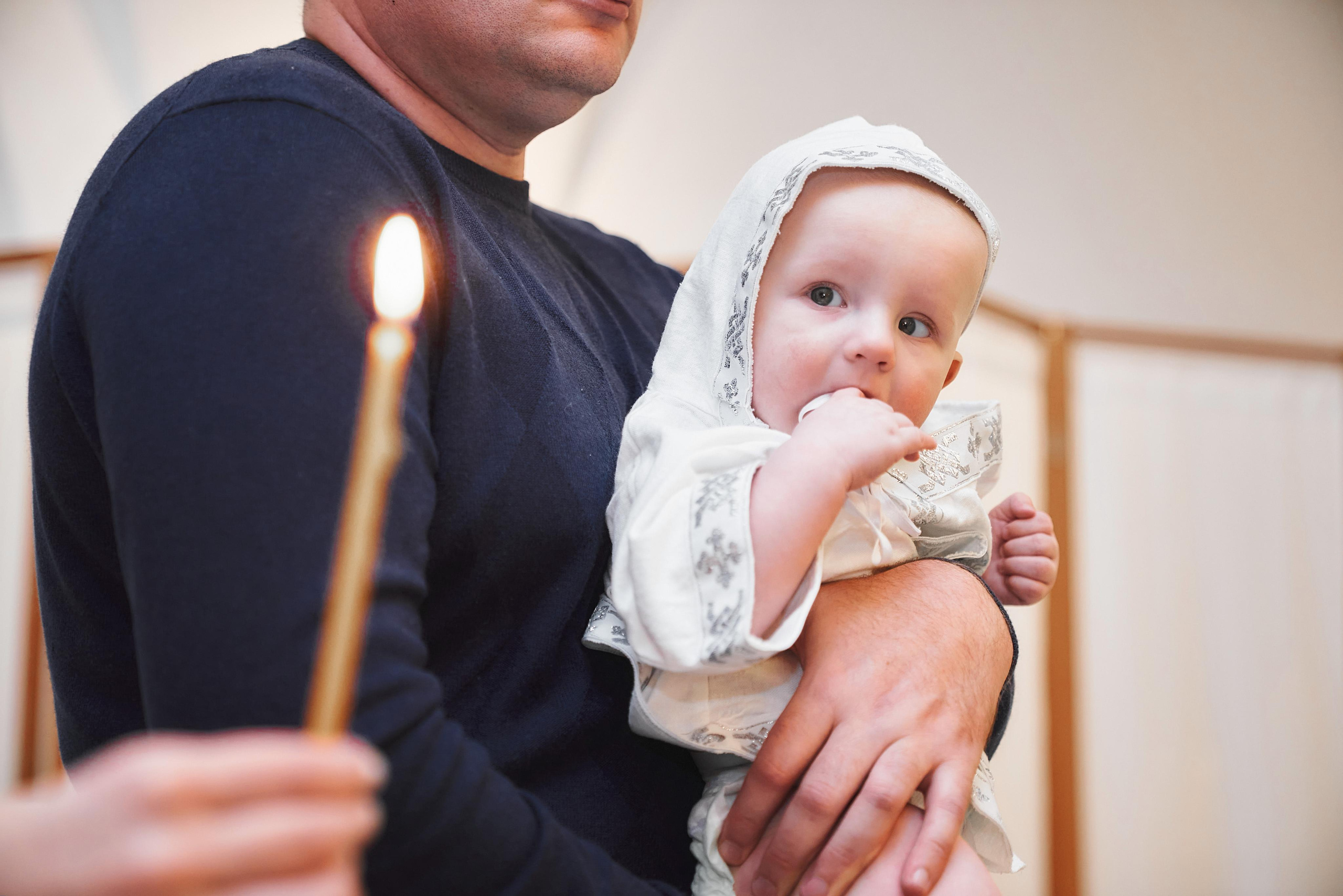 Ребёнок на руках у крёстного отца на крещении