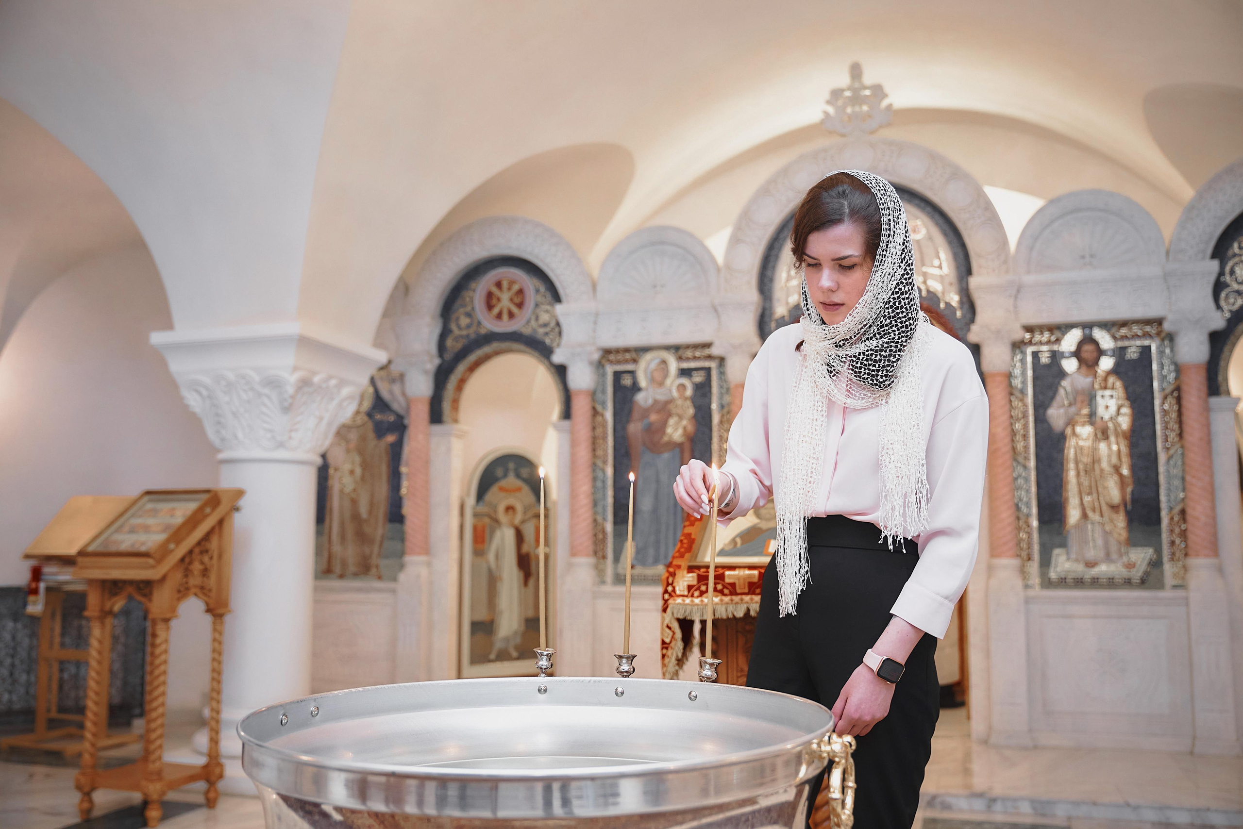 девушка в платке зажигает свечи на купели для крещения младенца