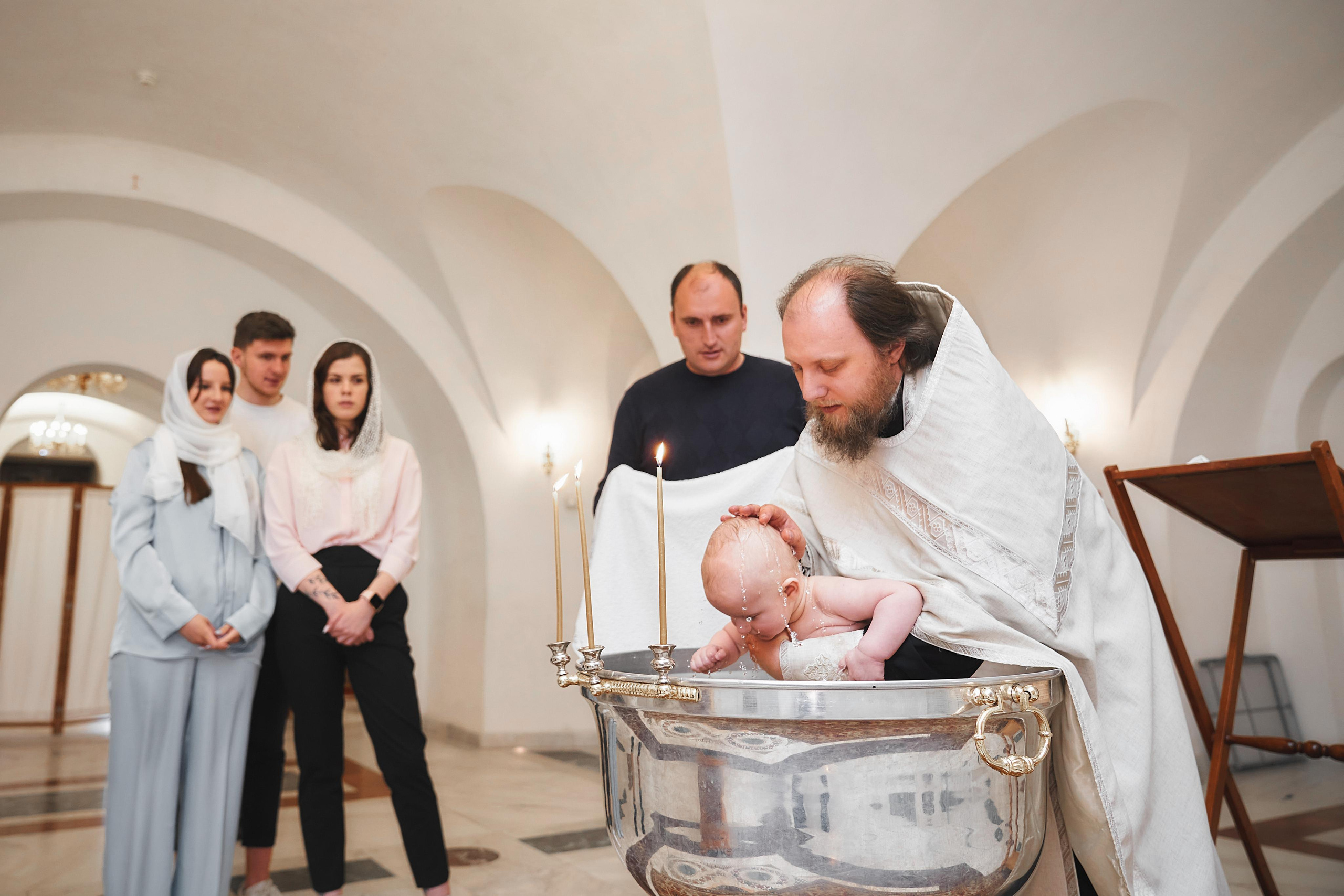 Ребёнка священник купает омывает в купели храма во время крещения