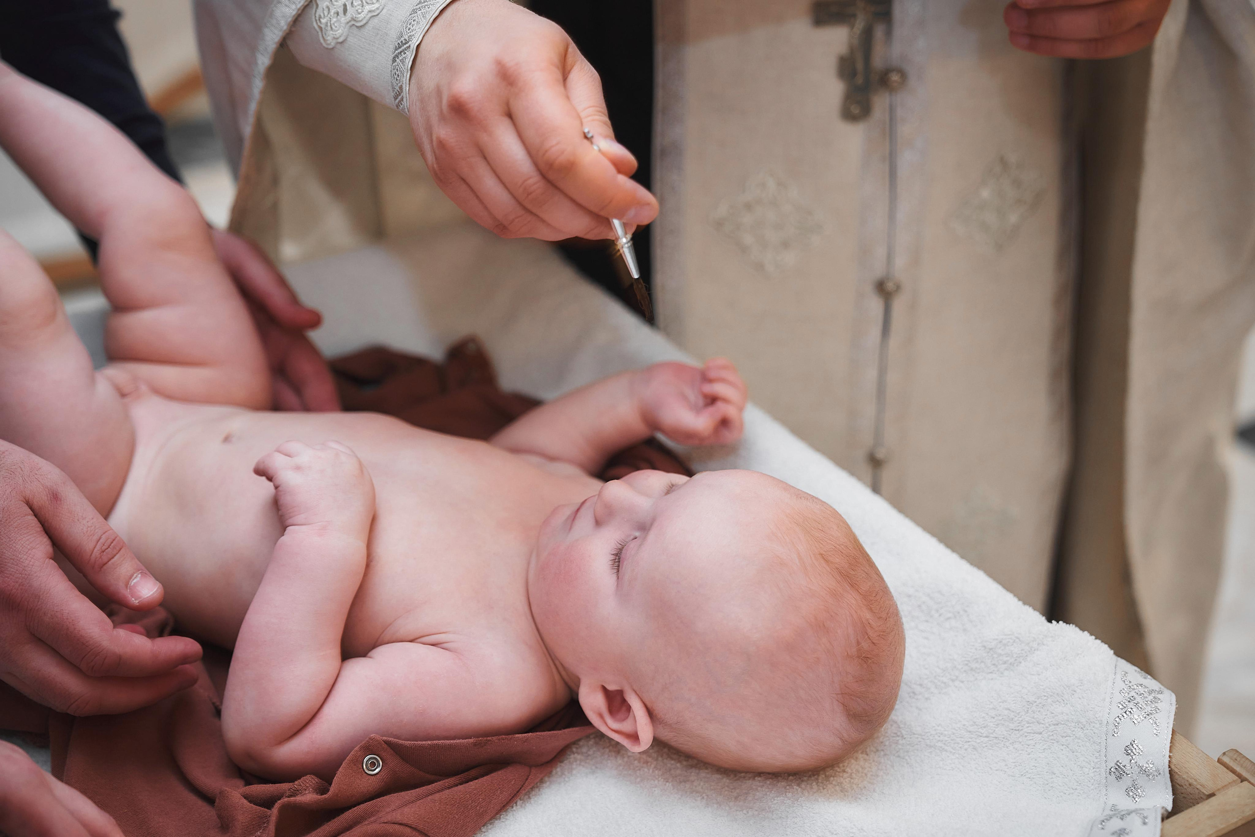 Священник помазывает ребёнка Миро на крещении