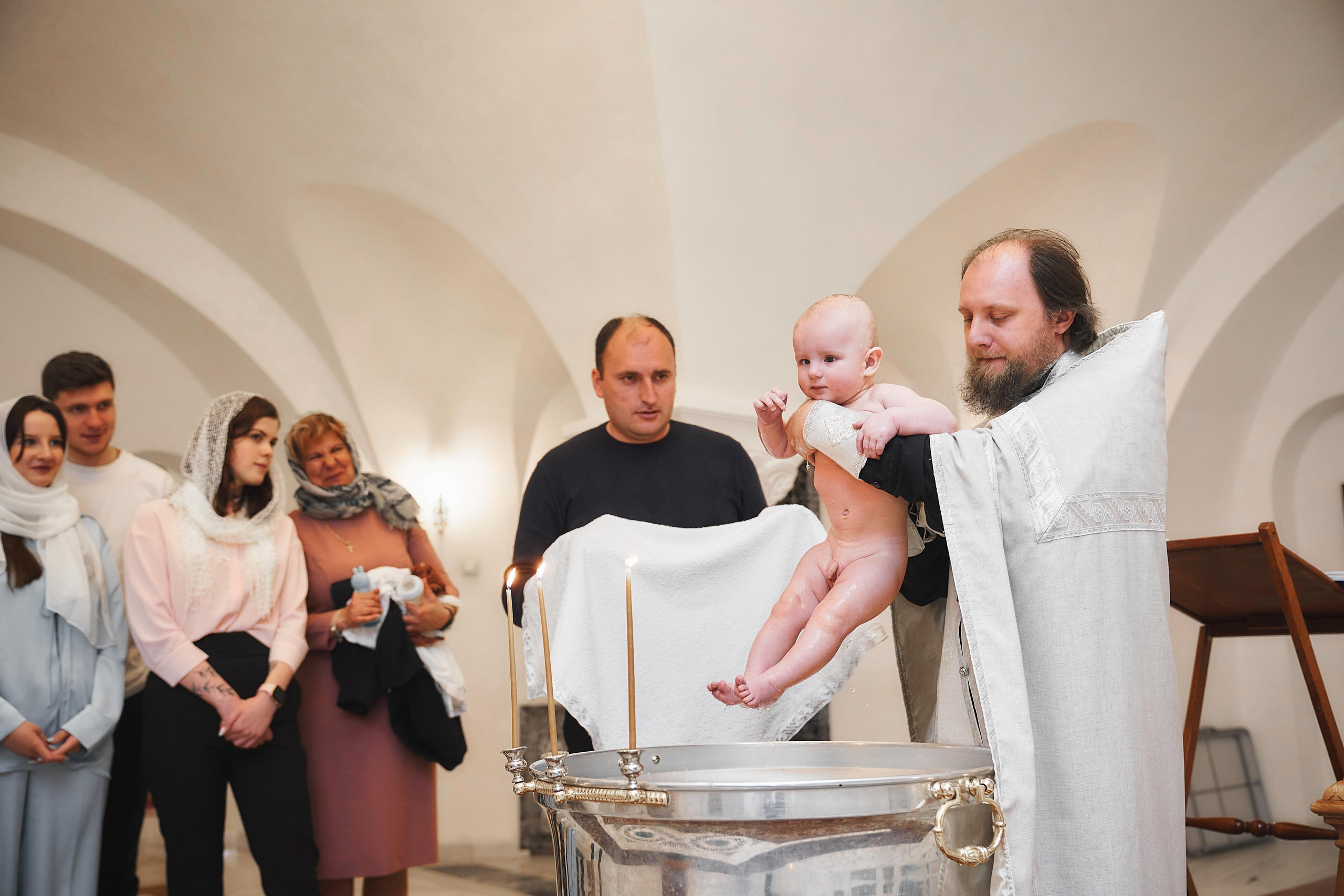 батюшка держит малыша над купелью после крещения