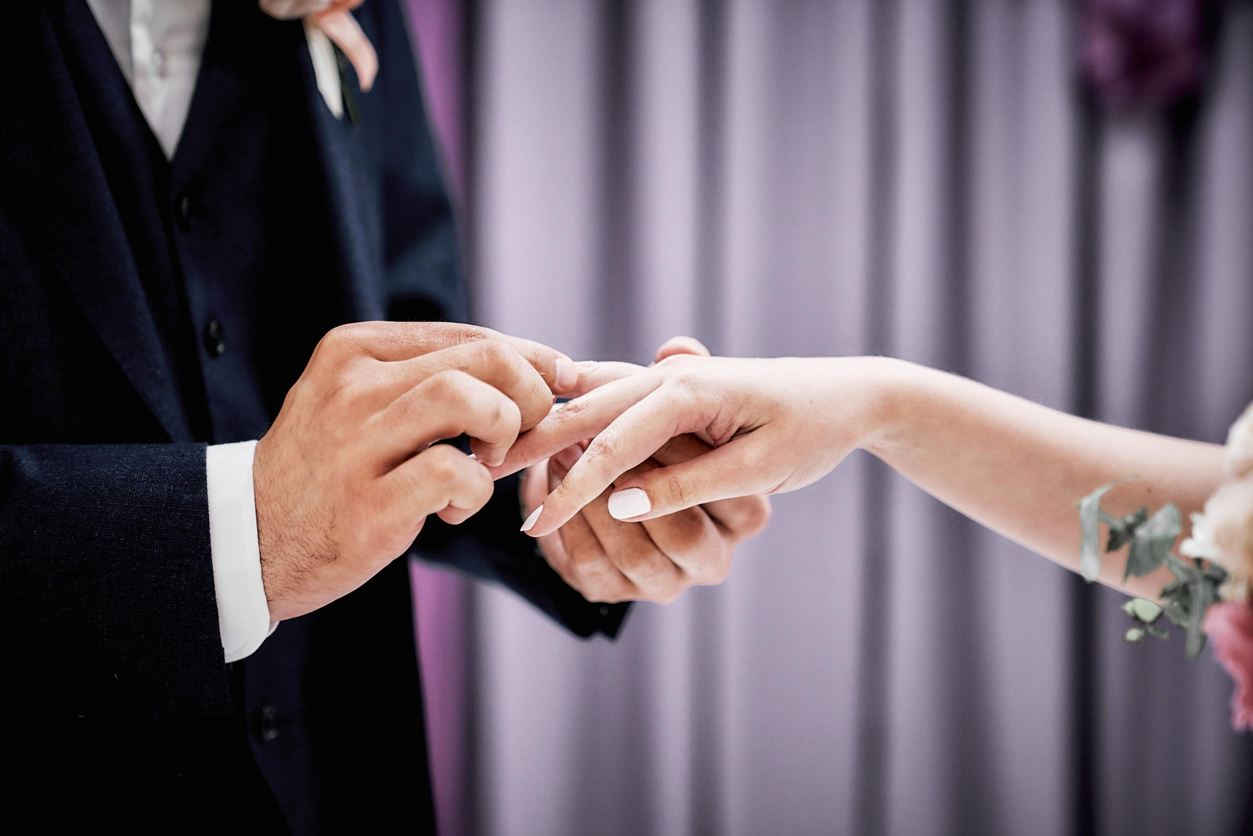 жених одевает кольцо на палец невесте, крупный план рук и обручального кольца