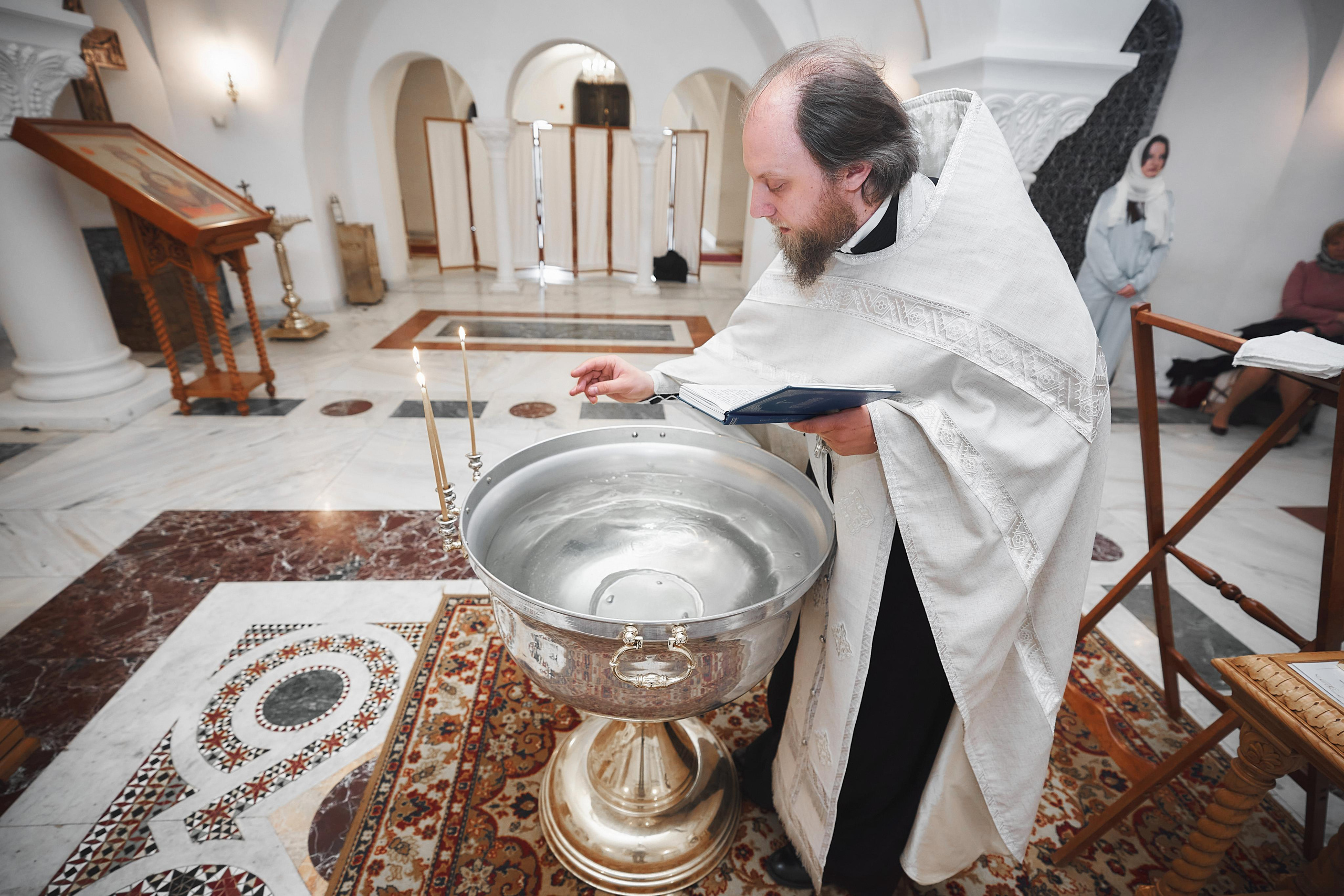 Батюшка освещает воду в купели для крещения ребёнка